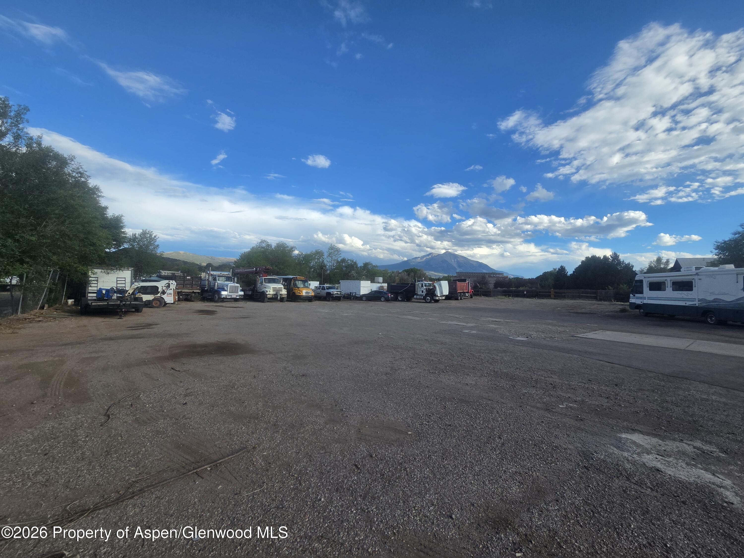 Gravel storage yard with parked work trucks and an RV, backed by mountains.