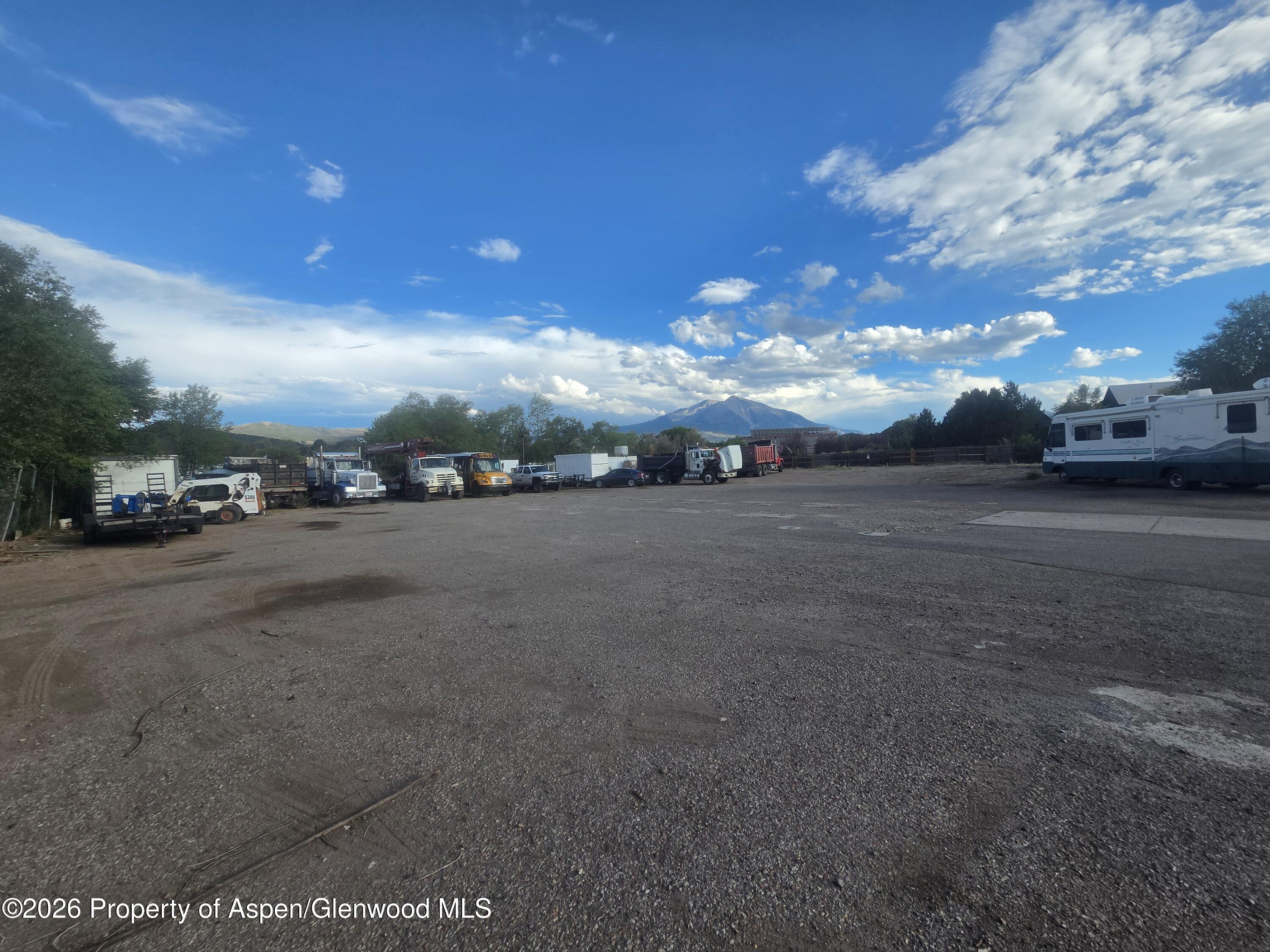 Gravel storage yard lined with work trucks and an RV, with mountains in the distance.