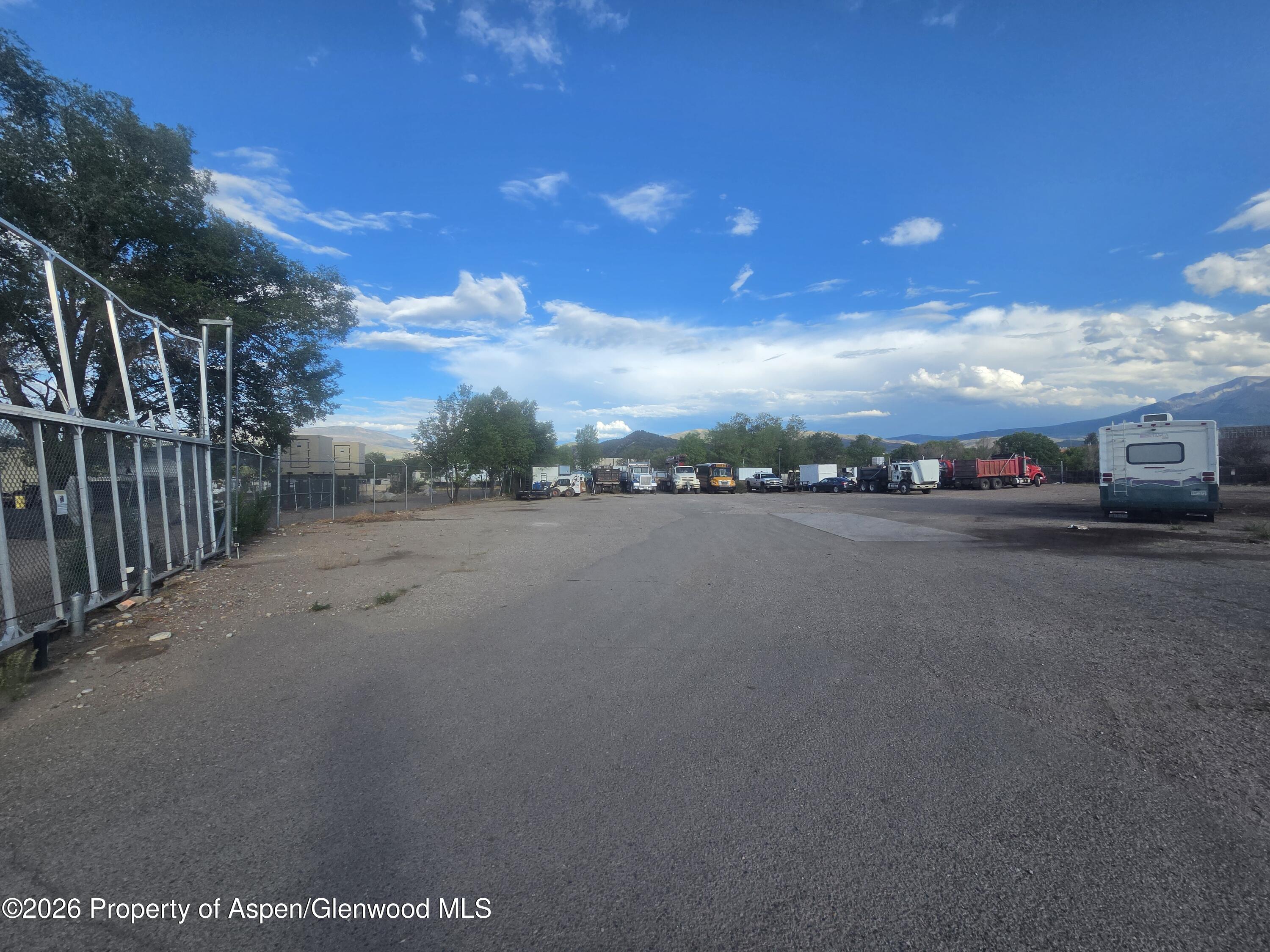 Yard storage lot with parked trucks and an RV, chain-link fencing, and mountains in the distance.