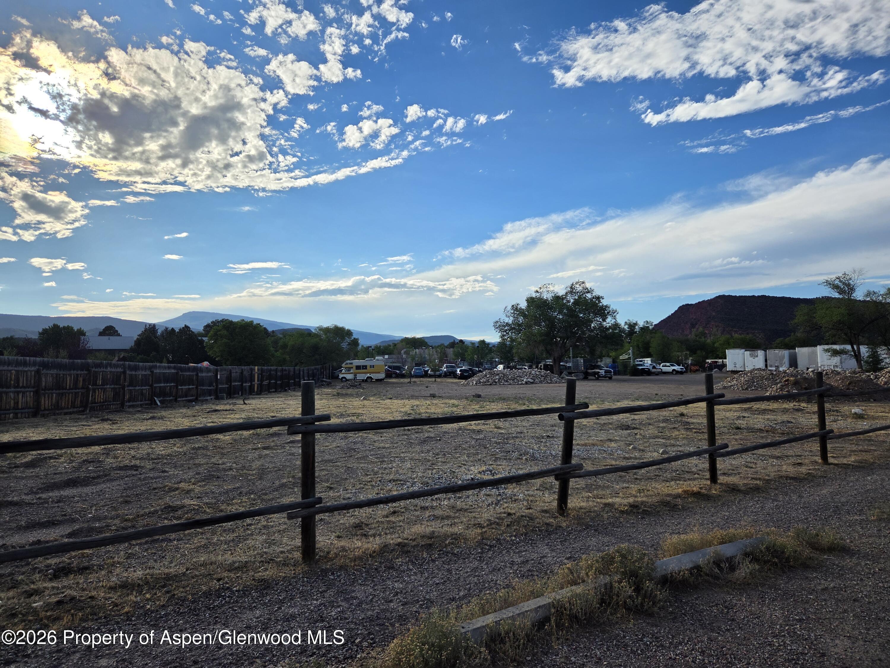 Fenced yard storage lot with parked vehicles, storage containers, and mountains in the distance.