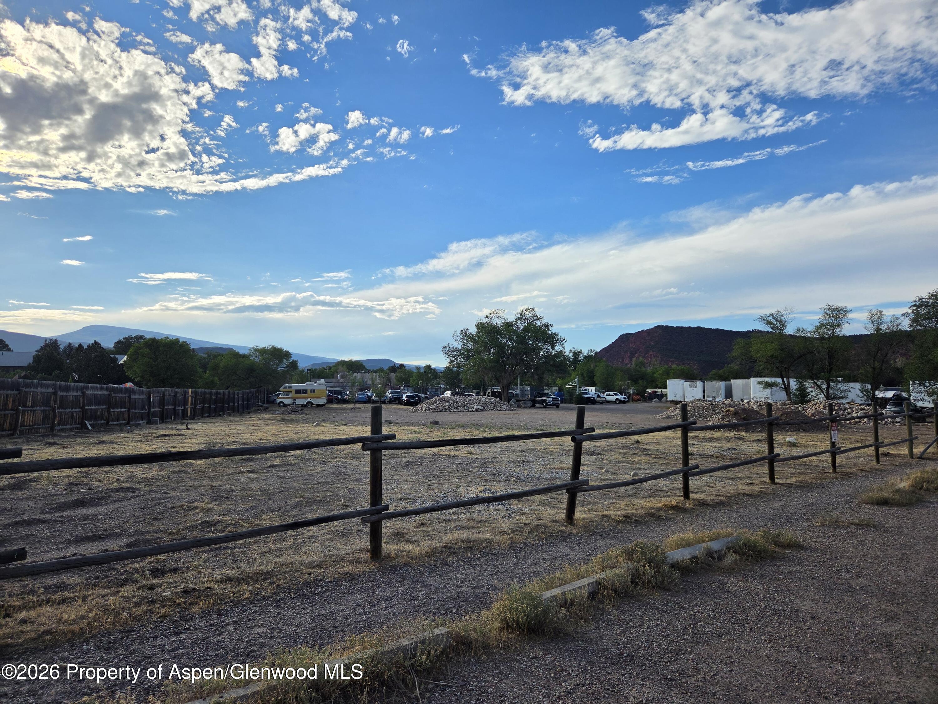 Gravel storage yard with rustic rail fencing, vehicles, storage containers, and mountains in the distance.