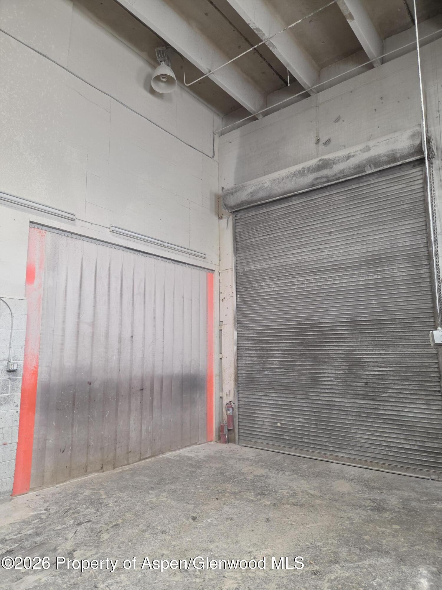 Industrial garage interior with a large roll-up door and red-edged strip curtain.