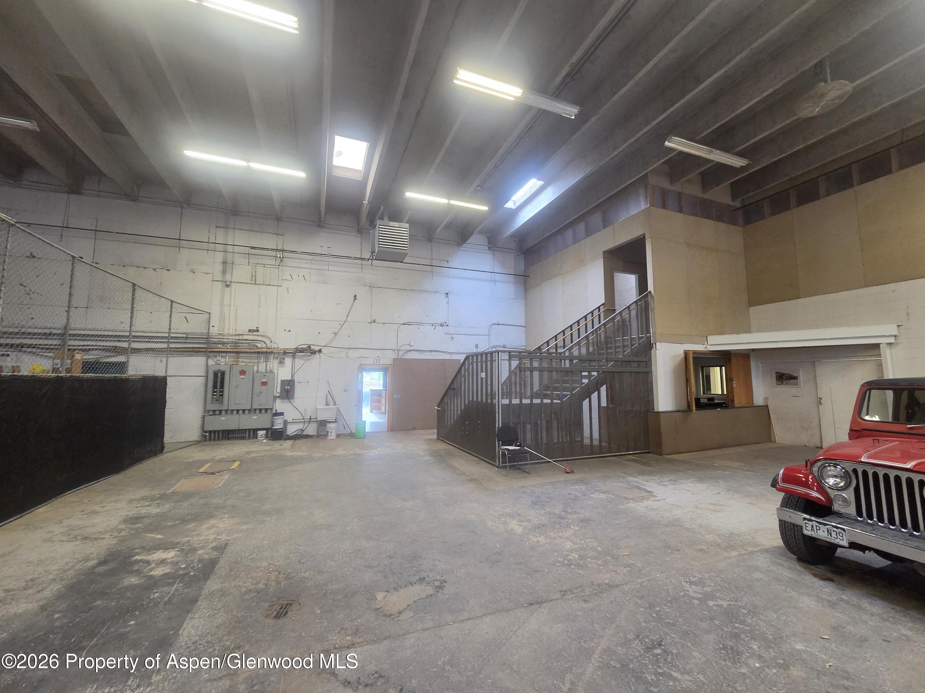 Industrial interior with a concrete floor, chain-link enclosure, metal staircase, and red Jeep.