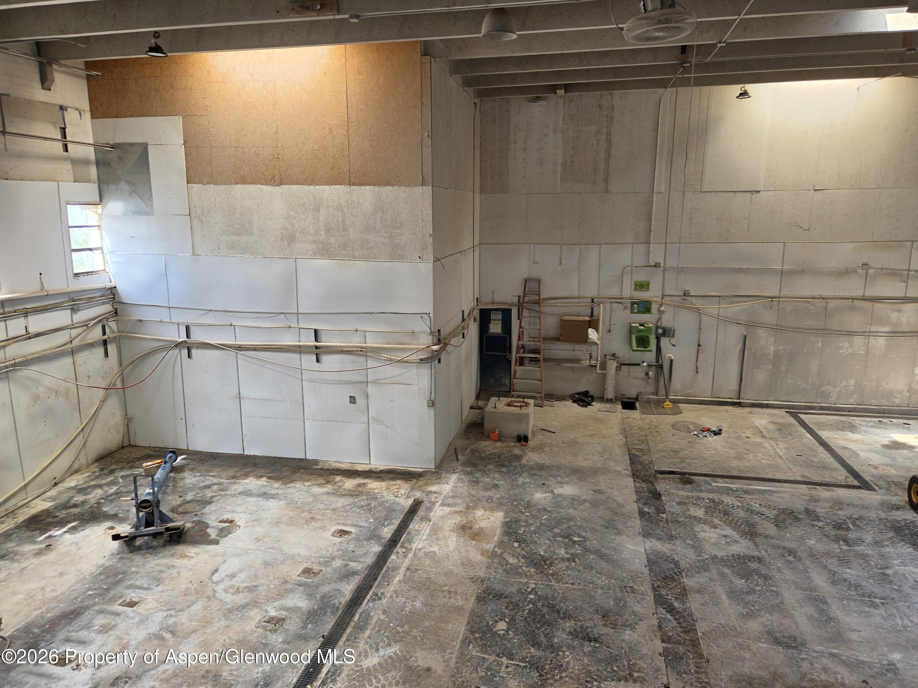 Large vacant workshop with exposed utilities, unfinished walls, and floor drainage channels.