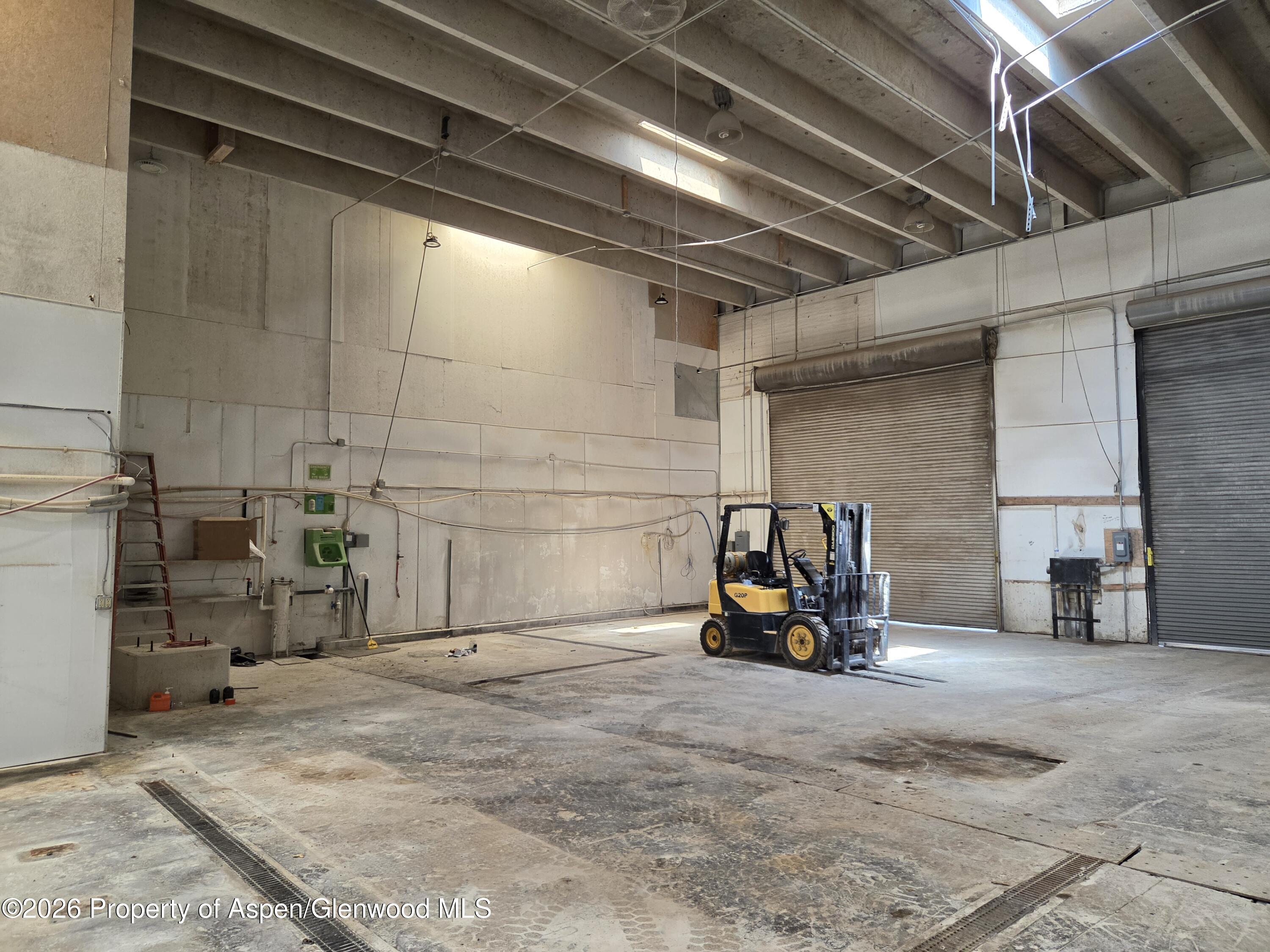 Industrial warehouse interior with a yellow forklift, concrete floor, and two roll-up doors.
