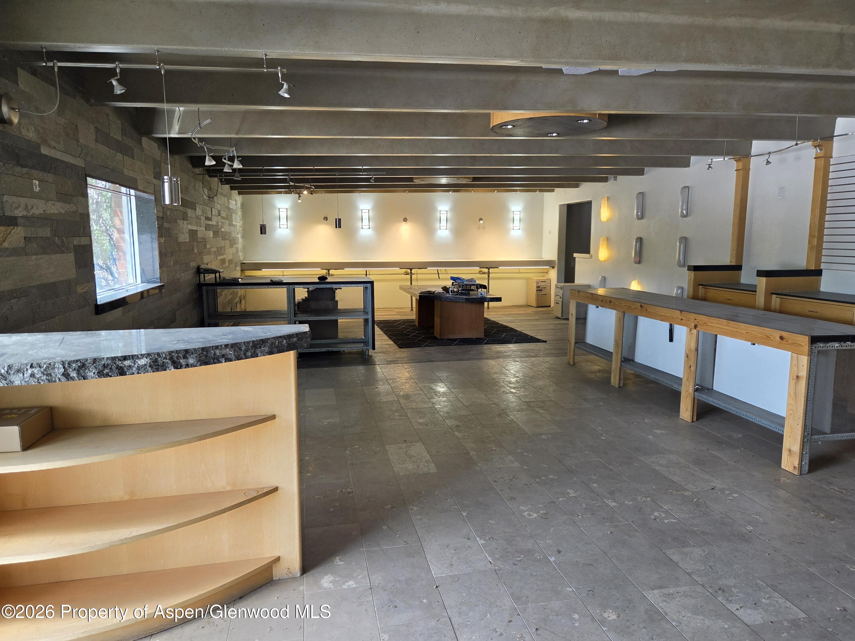 Vacant commercial interior with tiled floors, built-in counters, and long wooden display tables.