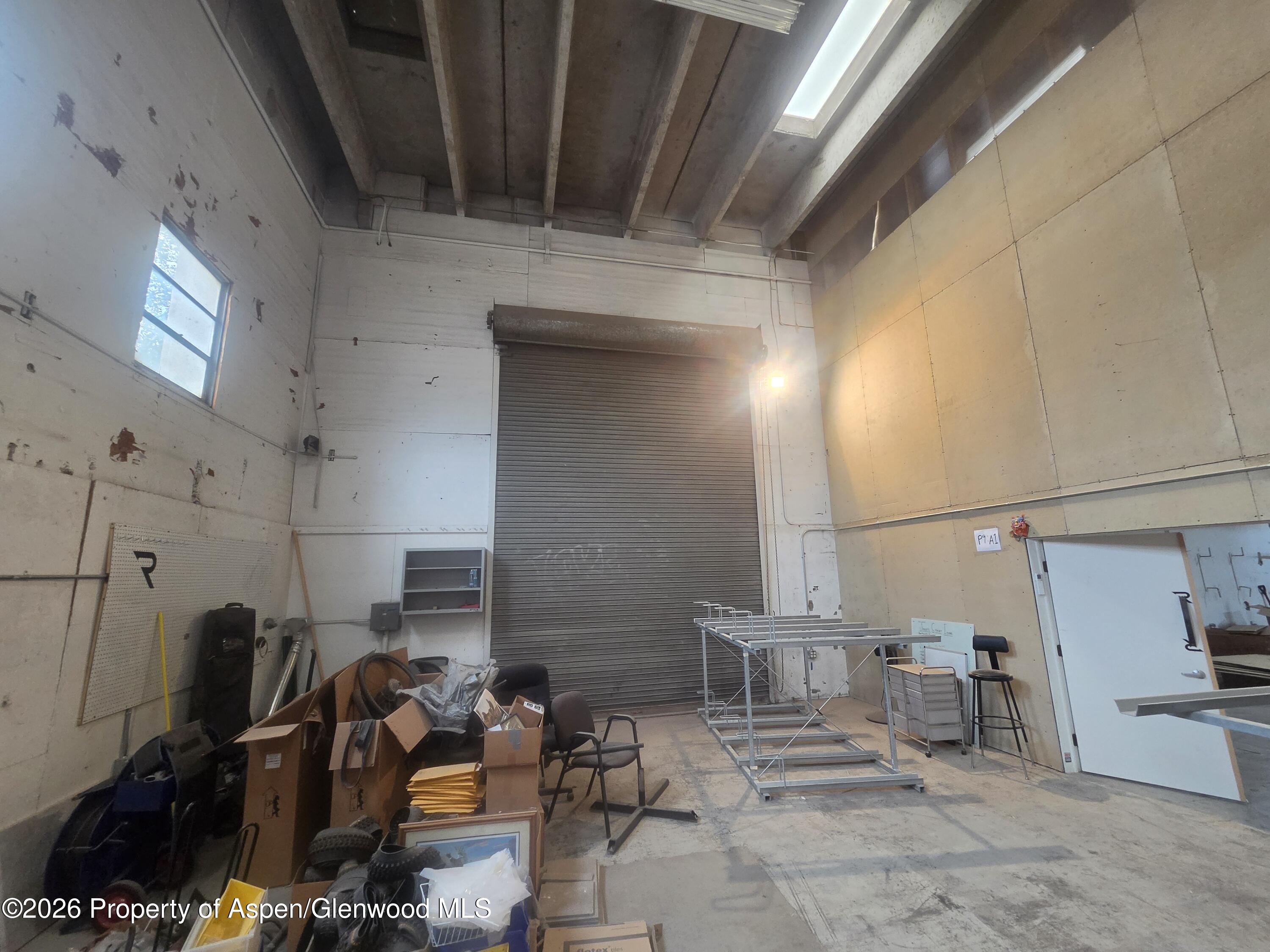 Industrial warehouse interior with a high ceiling, skylight, and large roll-up door.