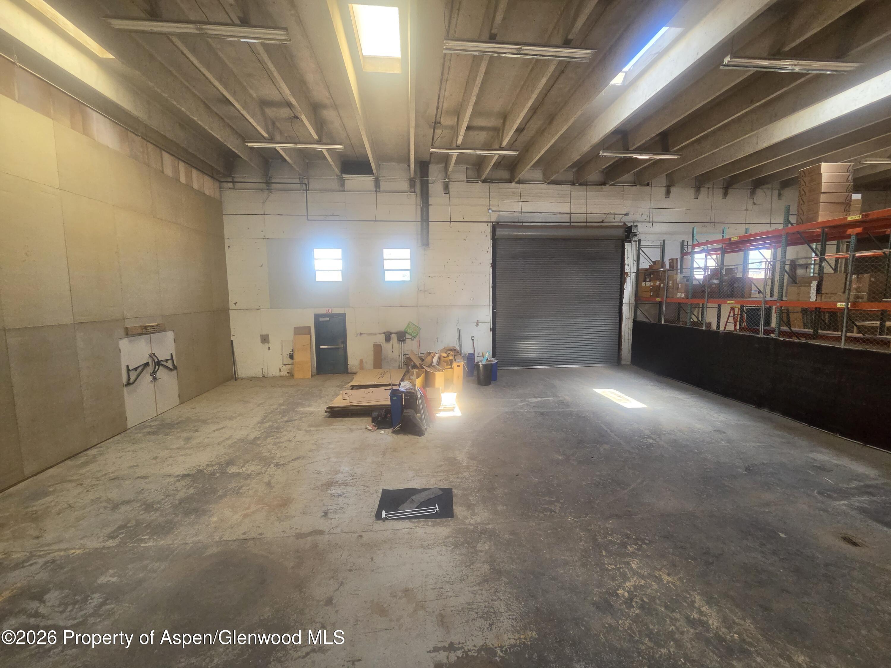 Large warehouse interior with exposed beams, a roll-up door, and fenced storage racks.