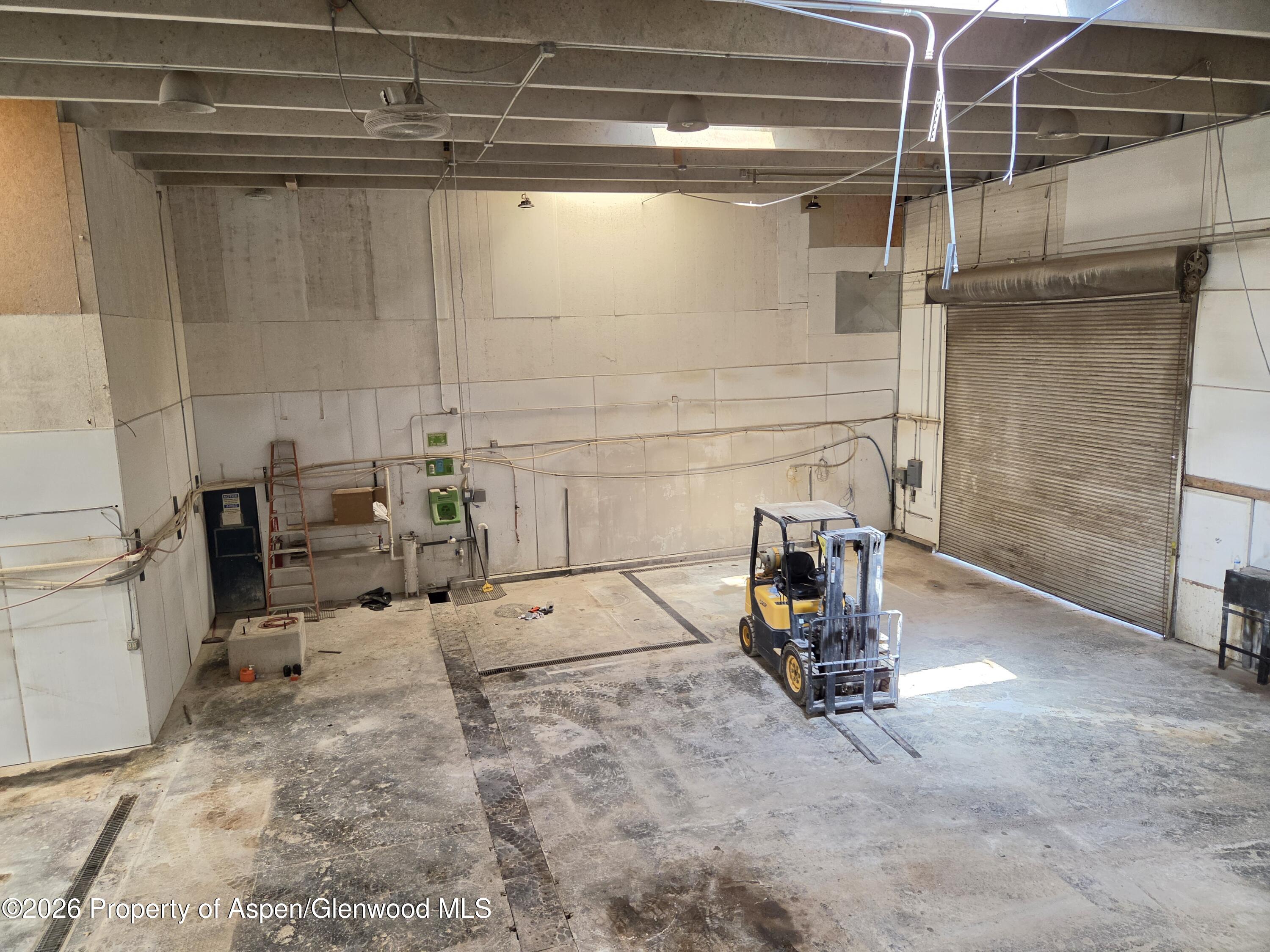 Industrial garage with a forklift, concrete floor, and closed roll-up door.