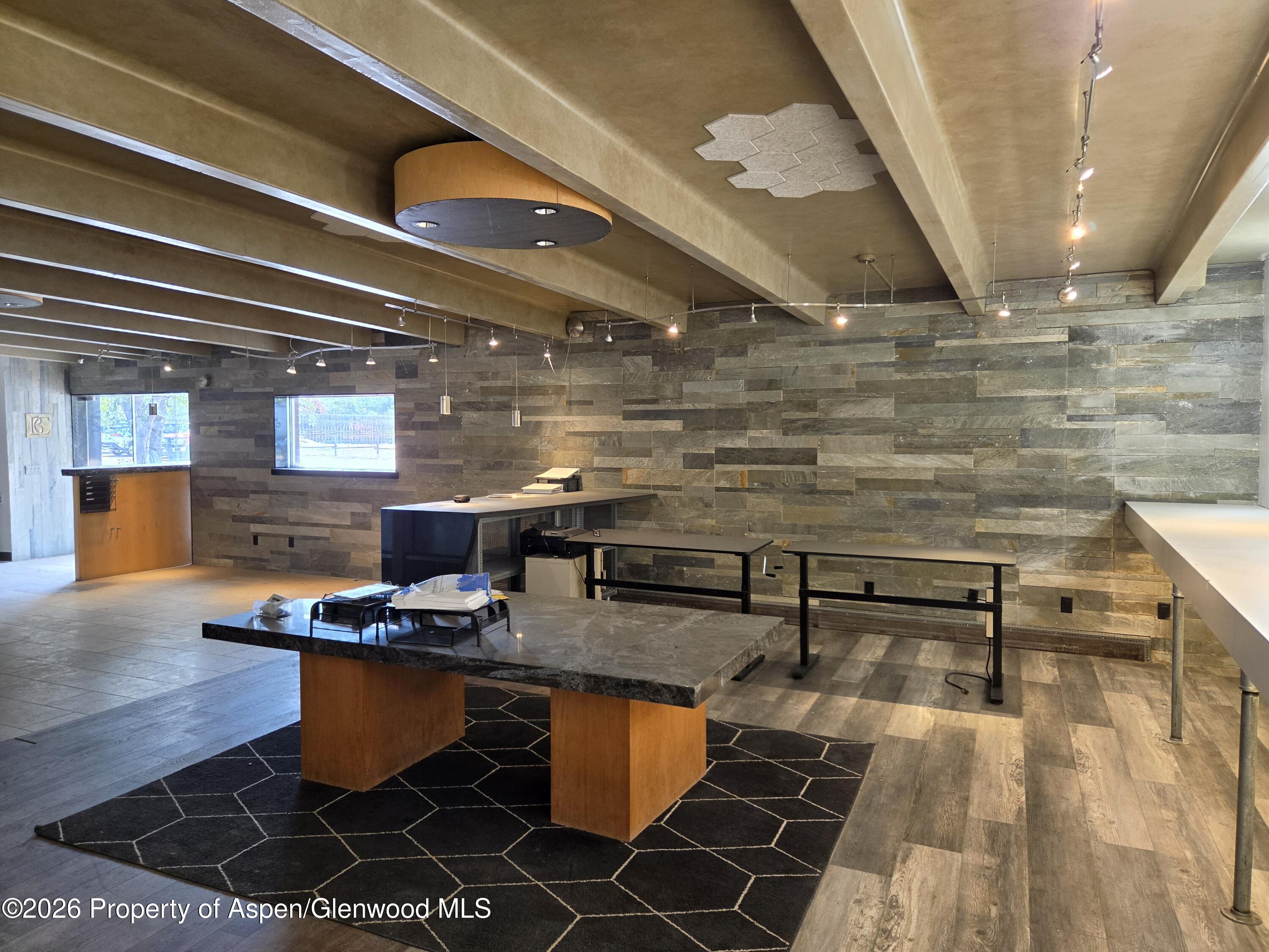 Workspace with stone-clad walls, exposed beams, and a large desk on a geometric rug.