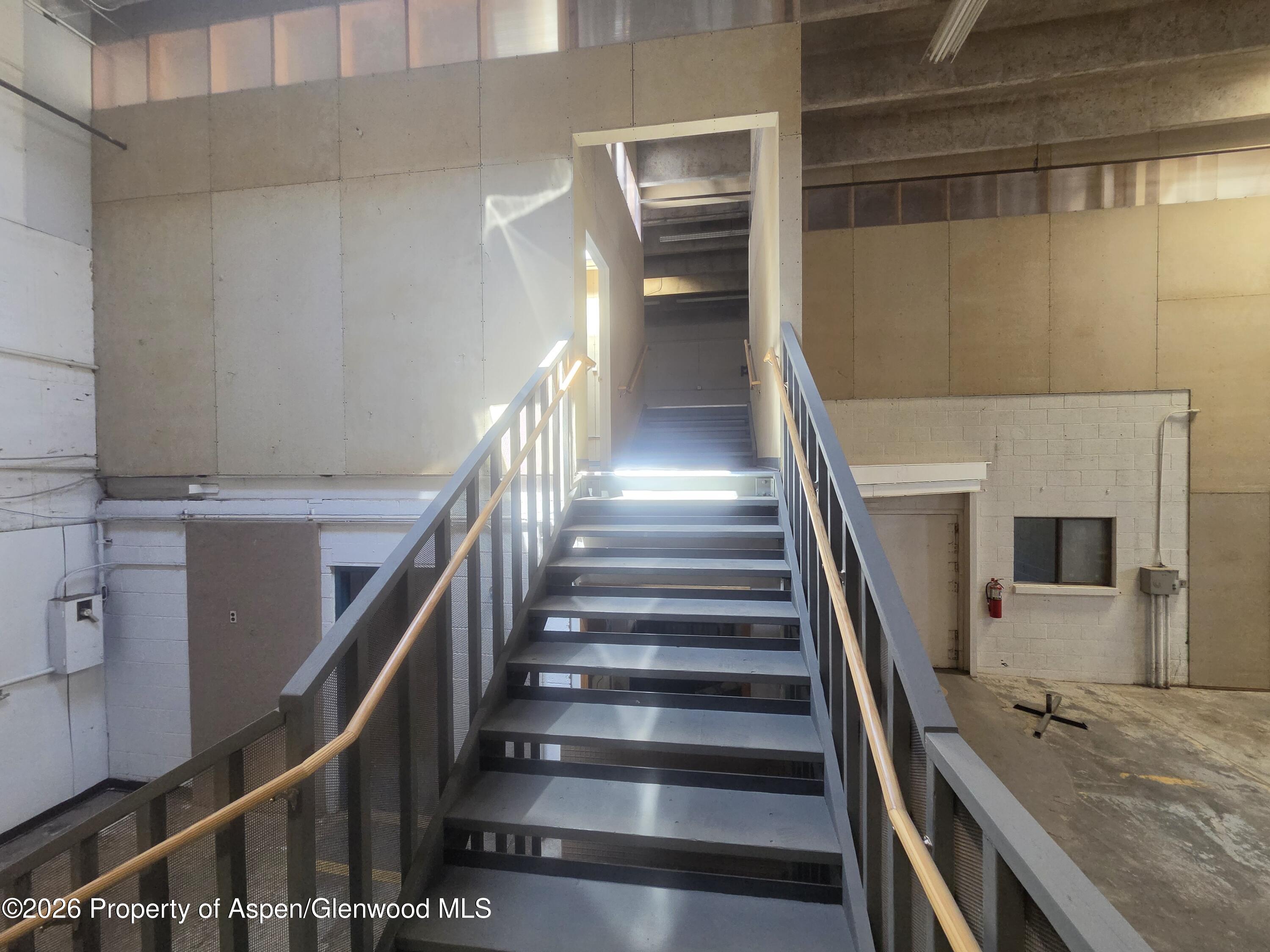 Industrial stairwell with open metal stairs, wooden handrails and sunlight across the steps.