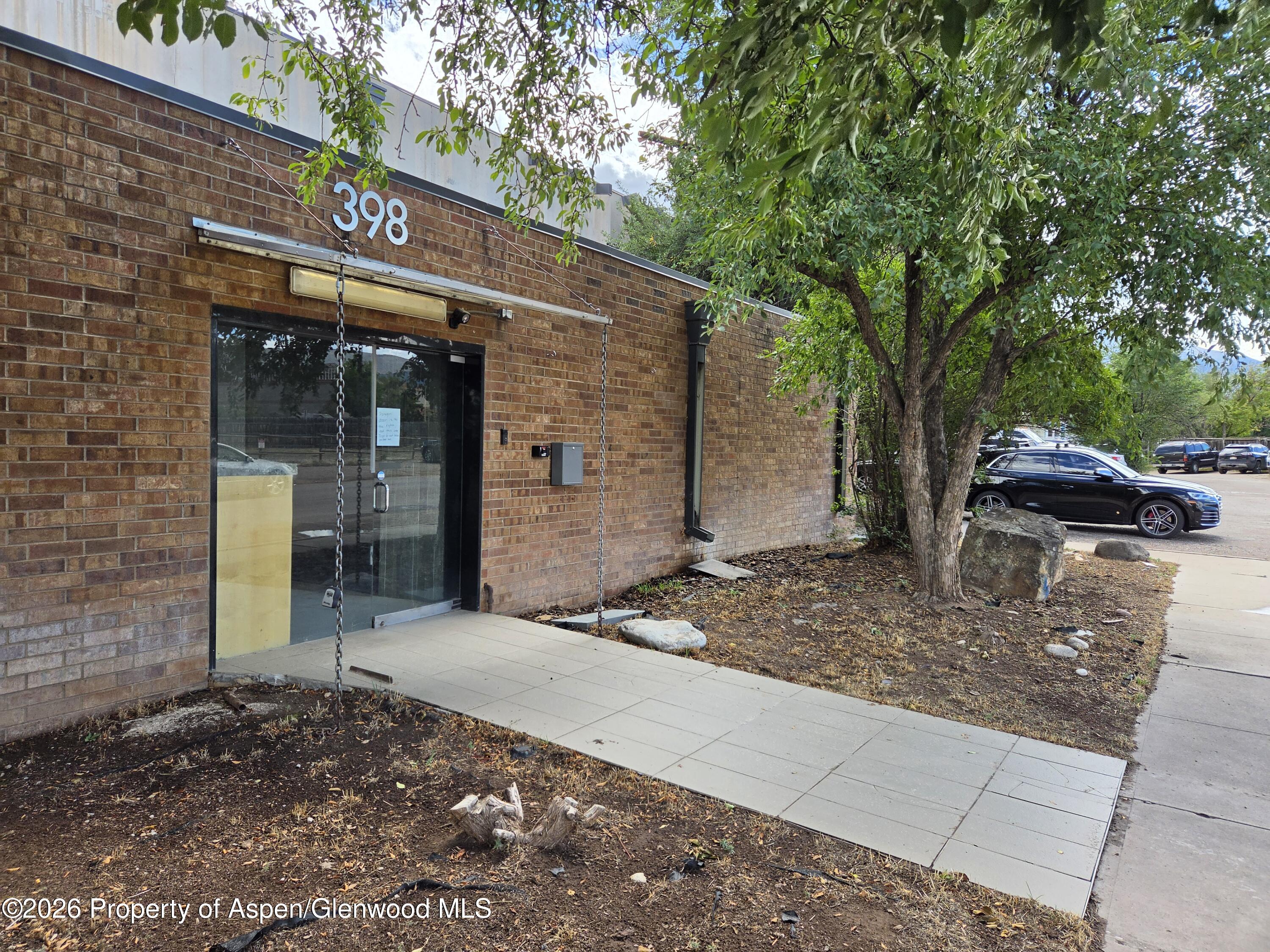 Brick commercial building entrance marked 398, shaded by a large tree beside the sidewalk.