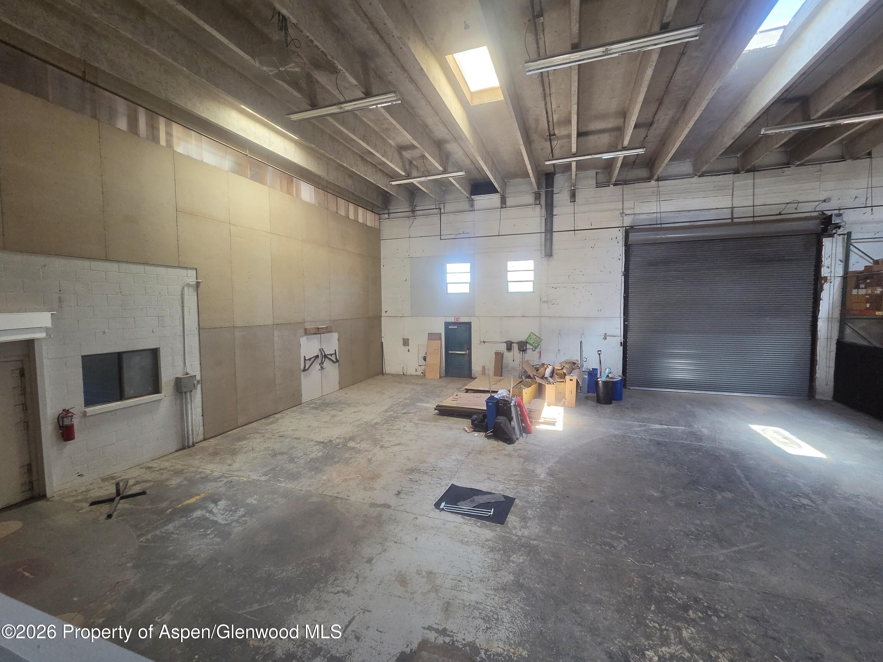 Warehouse interior with a high exposed ceiling, skylight, and closed roll-up door.