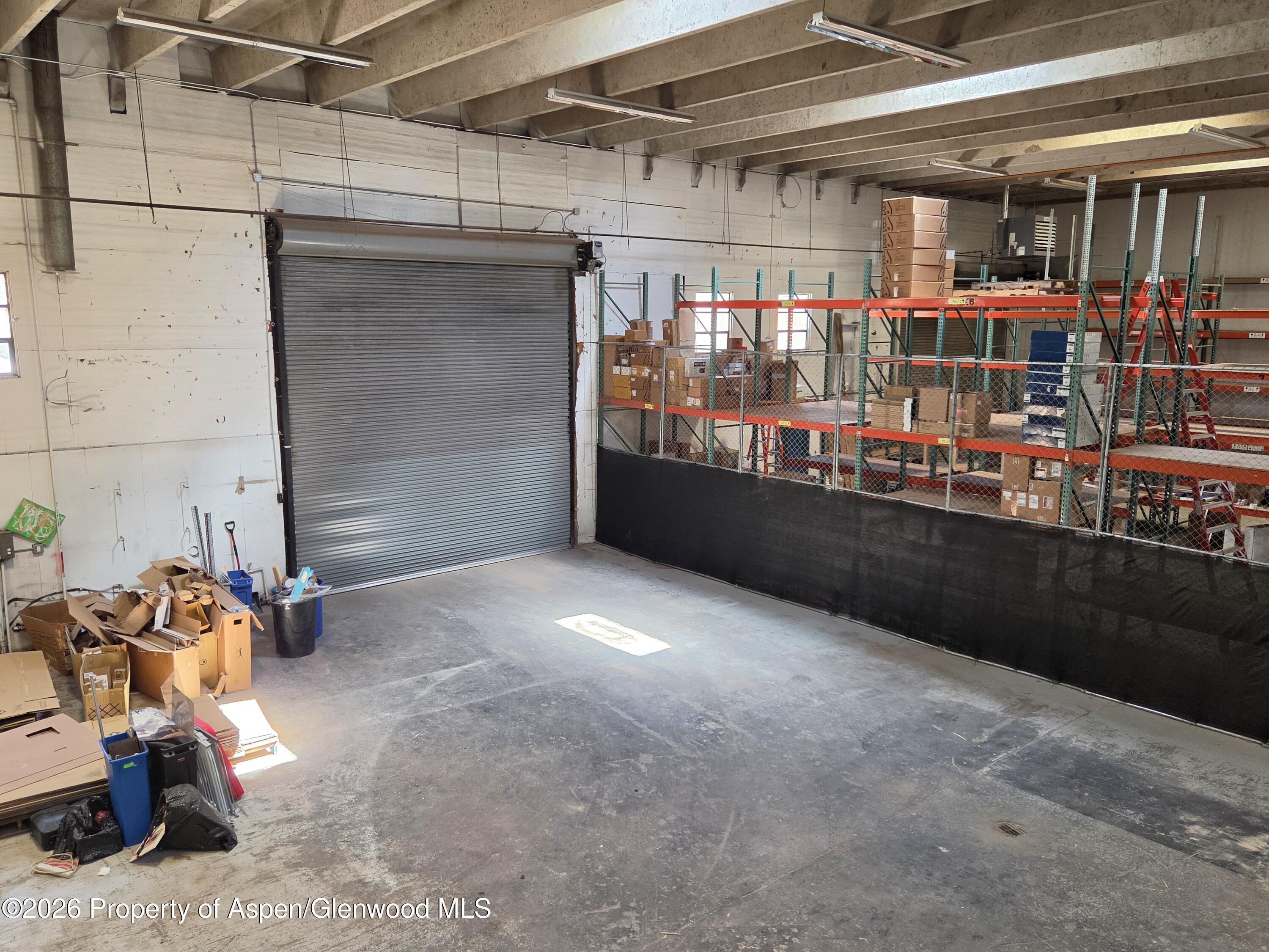 Commercial warehouse interior with a roll-up door and fenced shelving filled with boxes.