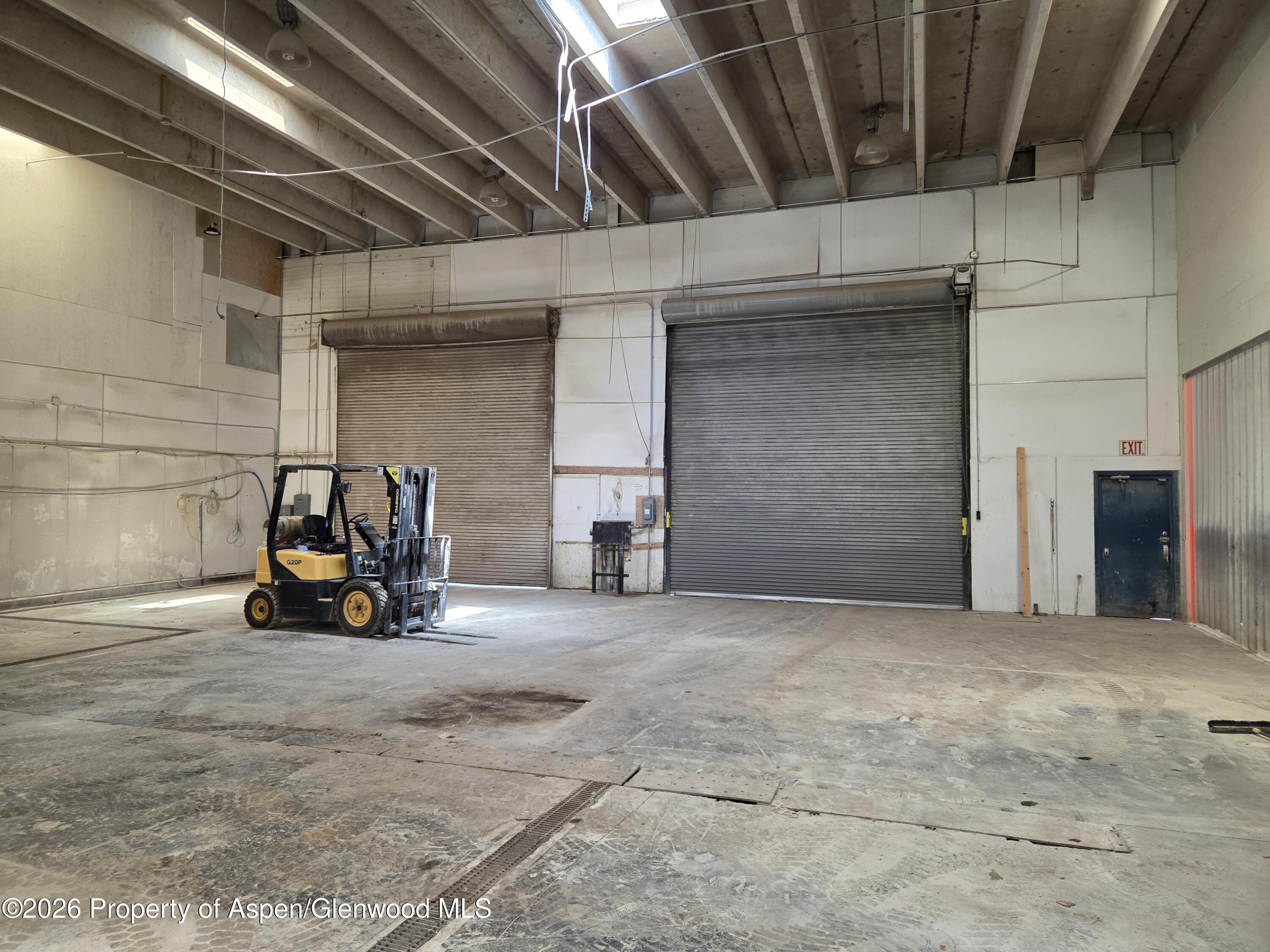 Warehouse interior with two roll-up doors, a yellow forklift, and exposed ceiling beams.