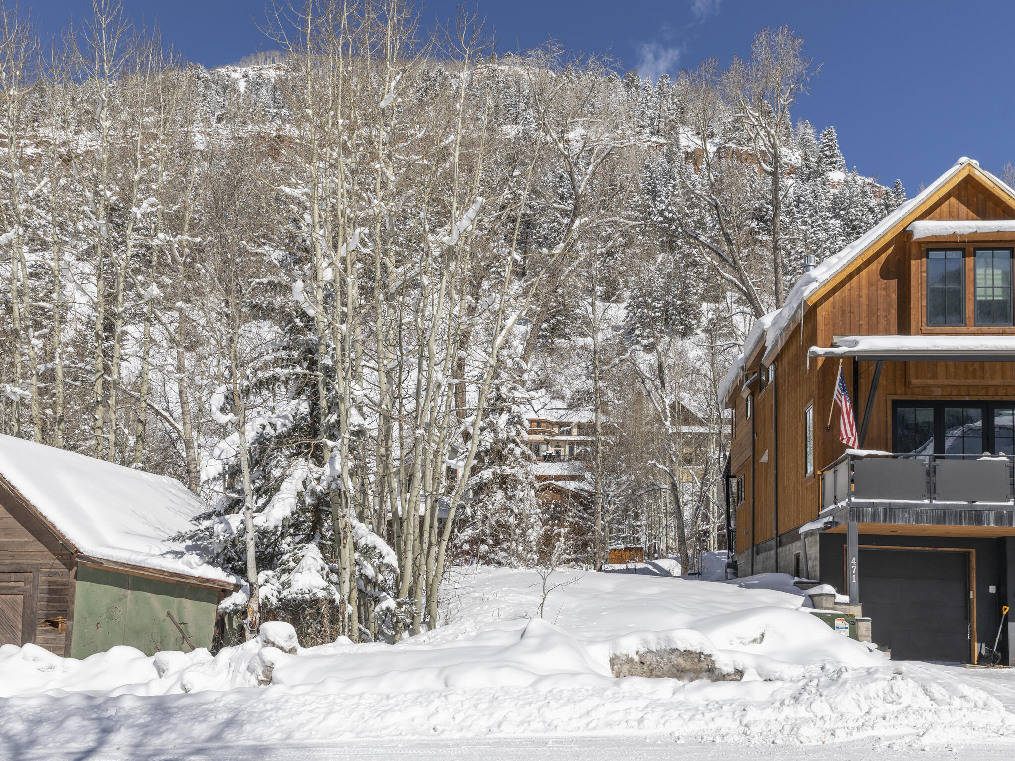 Wood-sided mountain home with a balcony and garage surrounded by deep snow and bare aspens.
