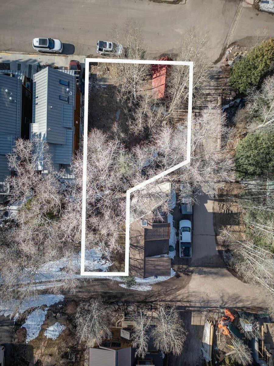 Aerial view of the outlined property parcel among homes, bare trees, and patches of snow.