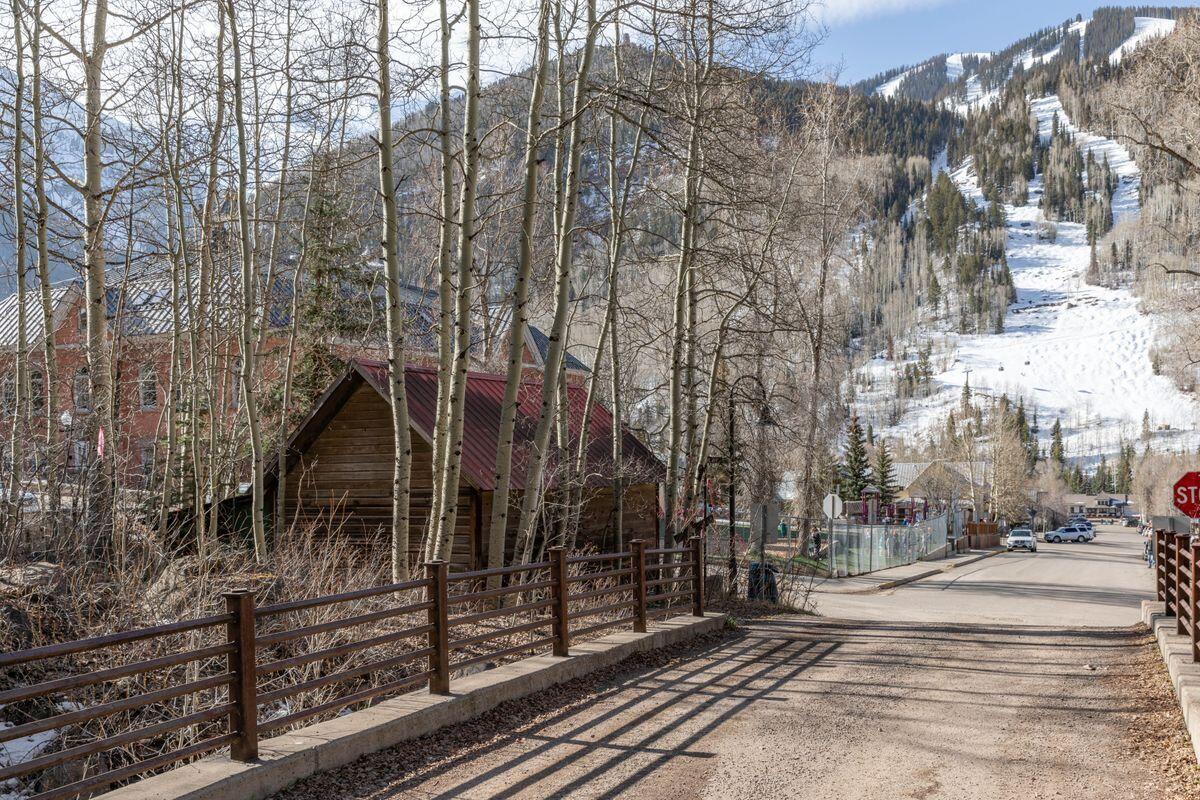 Wooden home behind a fence, with leafless aspens and a snowy ski run on the mountain.