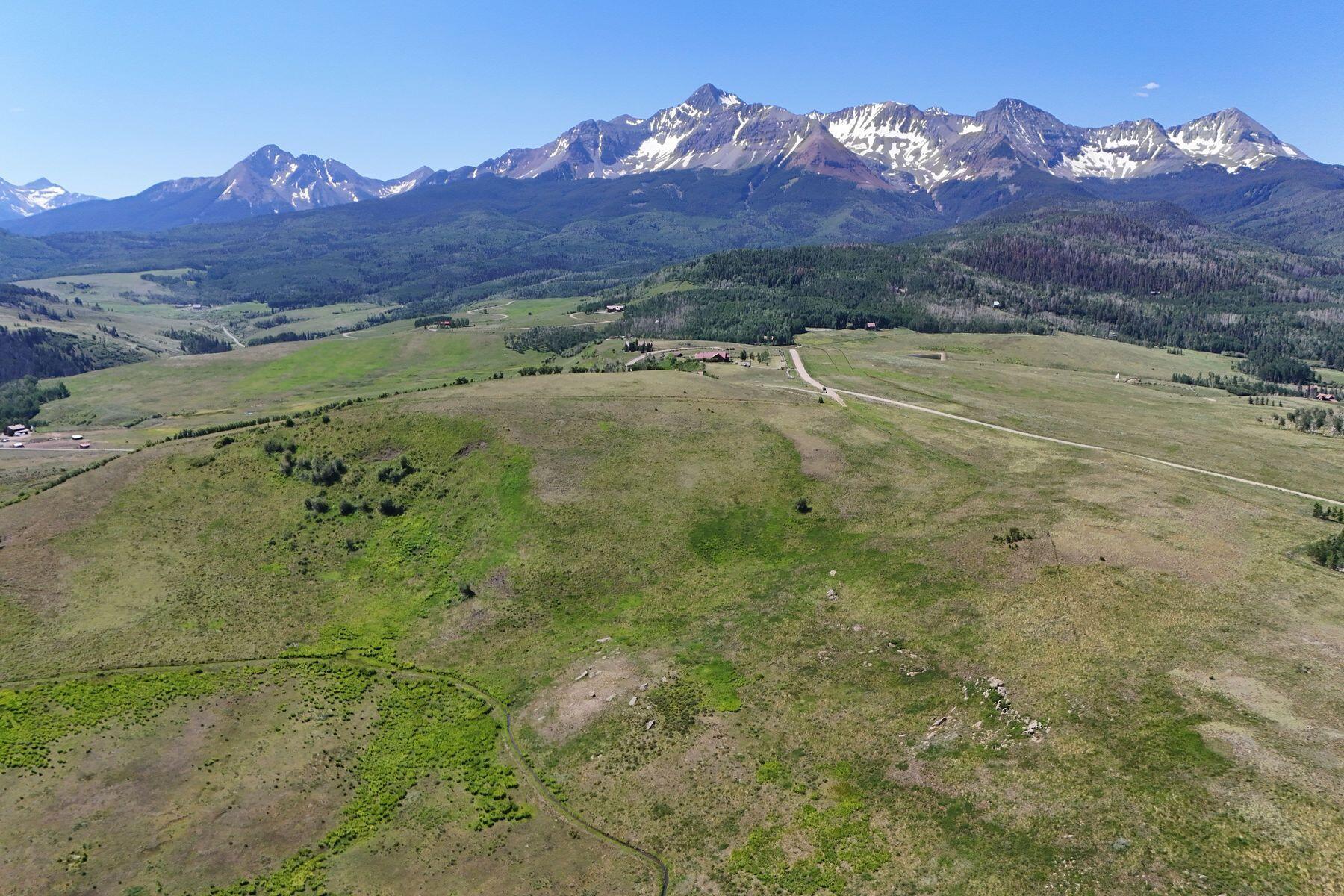 Aerial view of open acreage and a winding road beneath a snow-streaked mountain range.