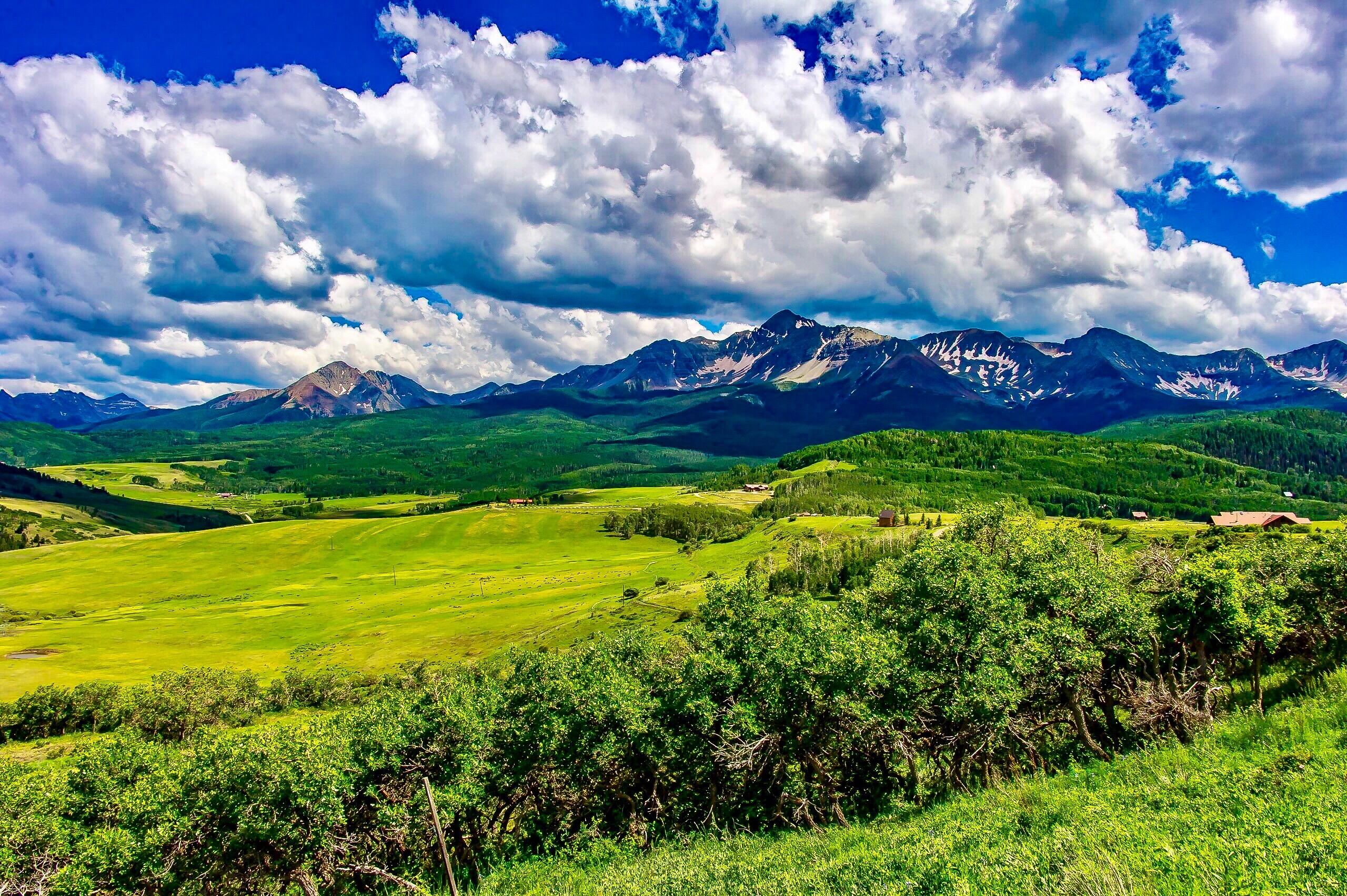 Open green fields and wooded hills with a distant mountain range beneath dramatic clouds.