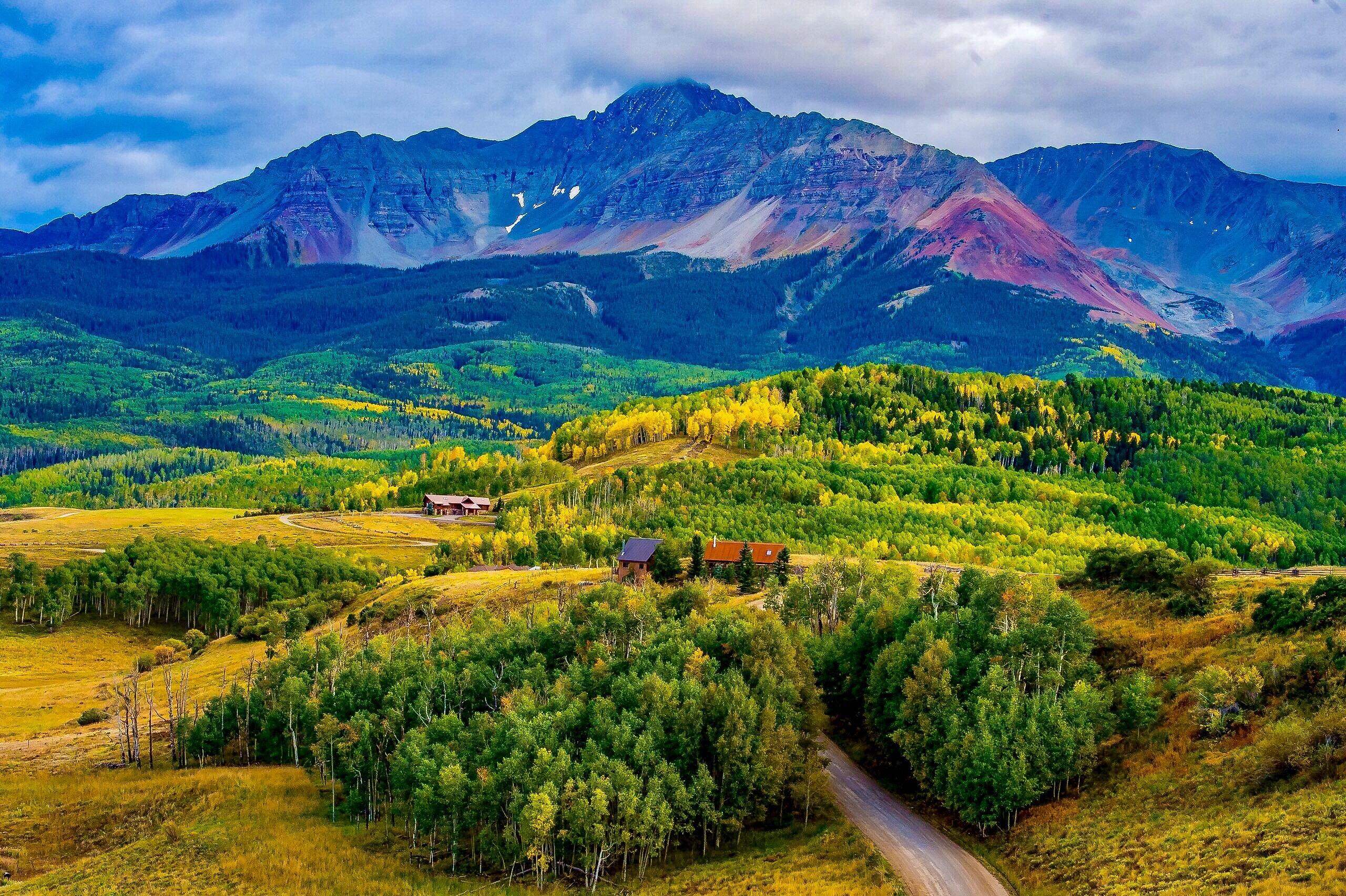 Rural property with scattered cabins, golden aspens, and a rugged mountain backdrop.
