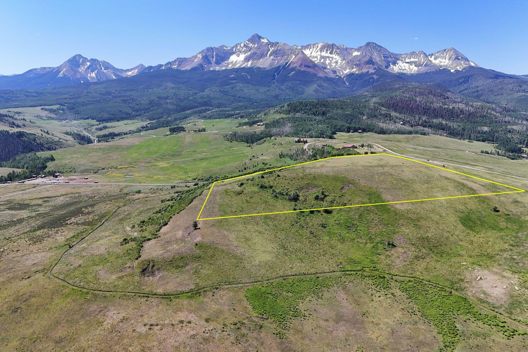 Aerial view of a vacant parcel outlined in yellow, with a snow-streaked mountain range beyond.
