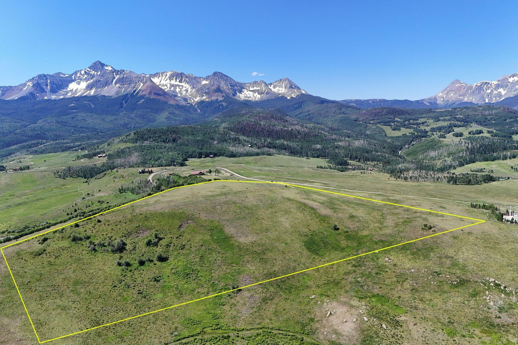 Undeveloped parcel outlined in yellow, with open grassland and snow-streaked mountains beyond.