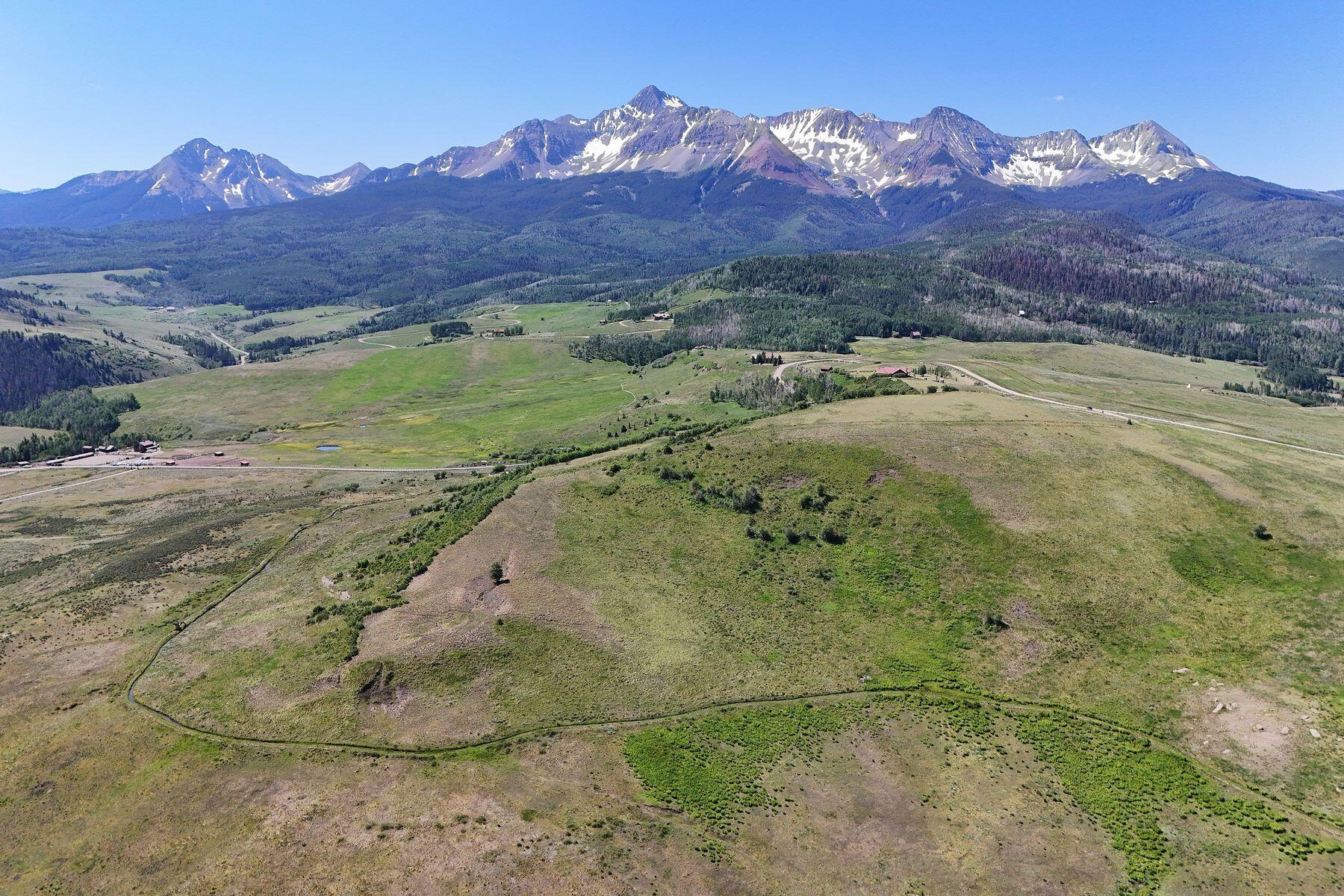 Aerial view of open meadowland with a sweeping snow-streaked mountain range beyond.