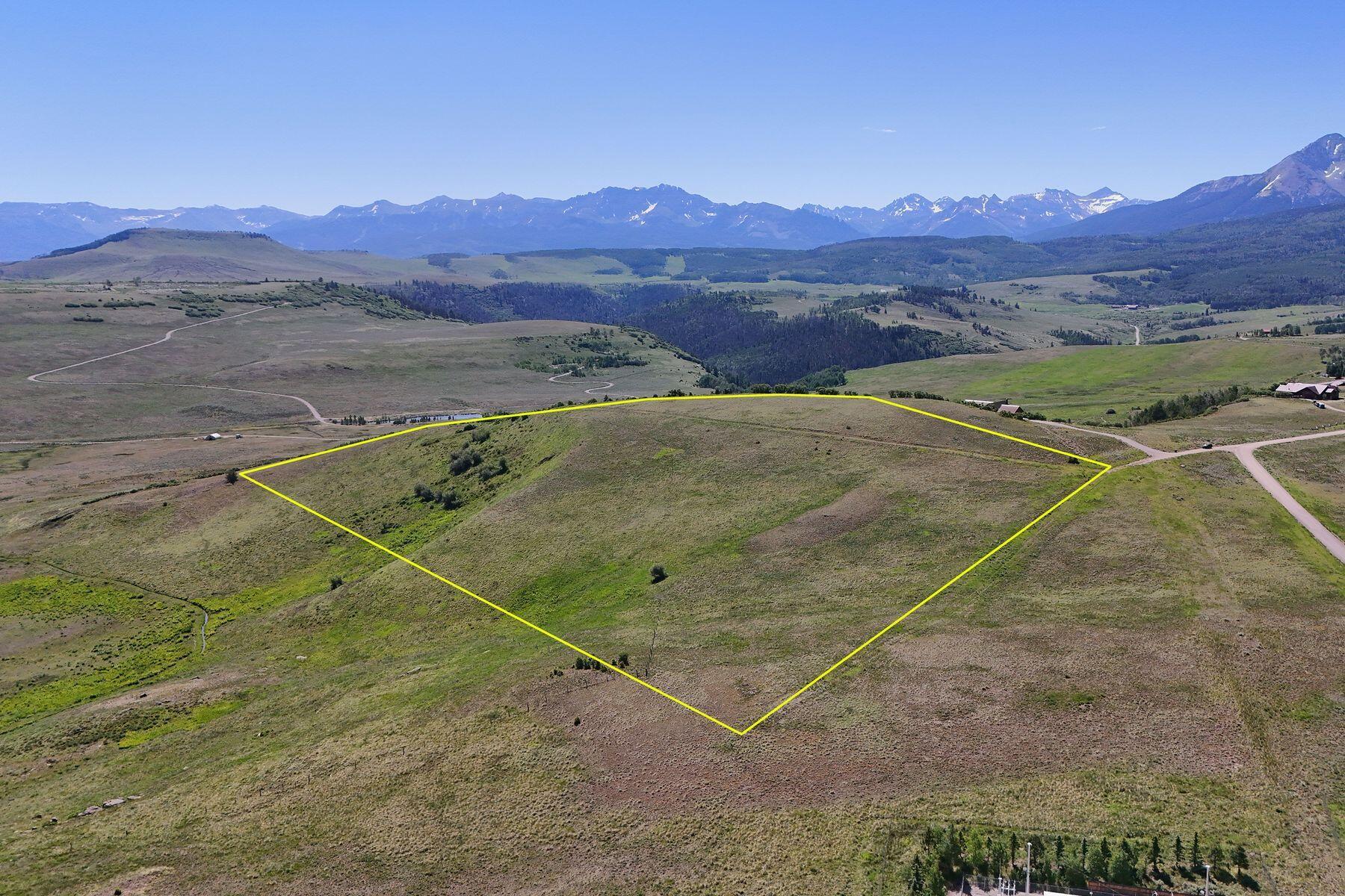 Vacant parcel outlined in yellow across open hills, with distant snow-dusted mountains.