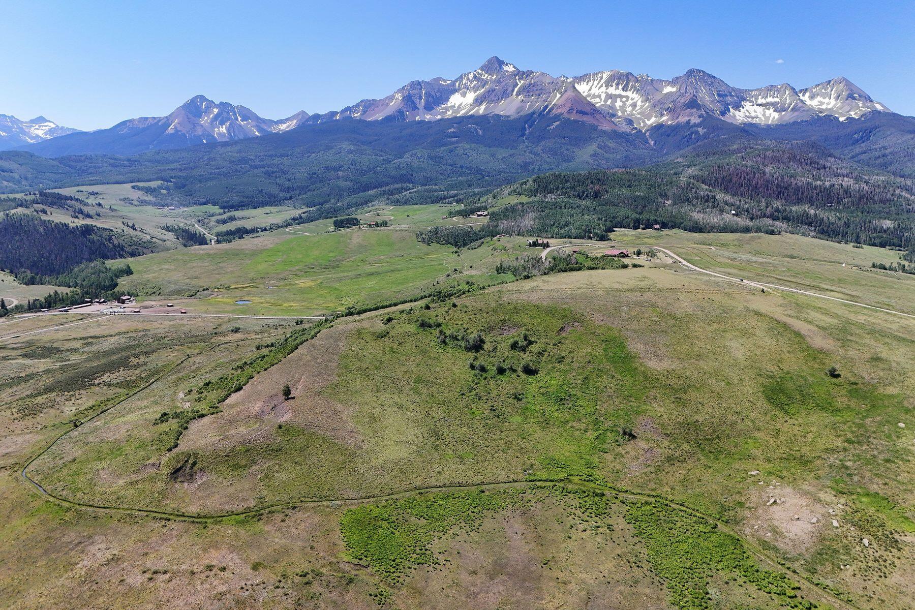Aerial view of open rural land with a broad snow-dusted mountain range beyond.