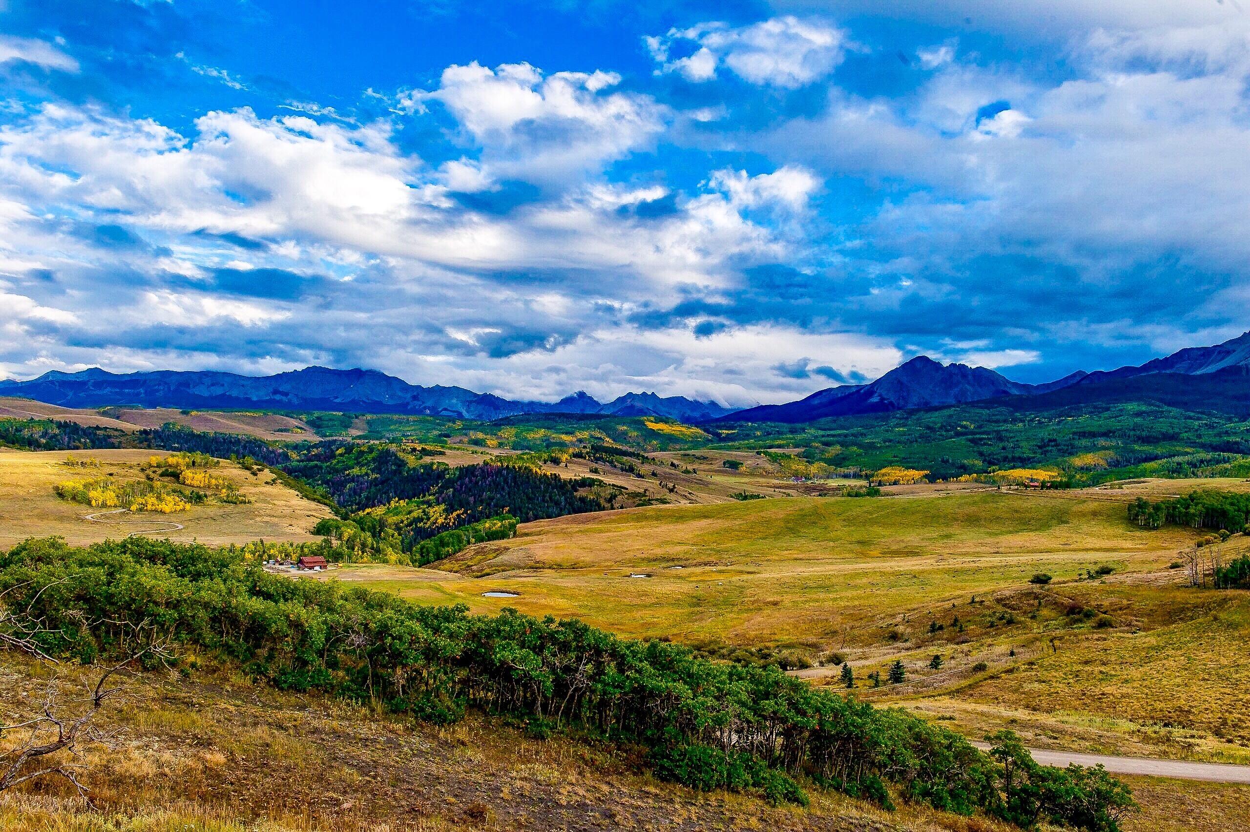 Rolling open land with scattered trees, a small pond, and distant mountains.