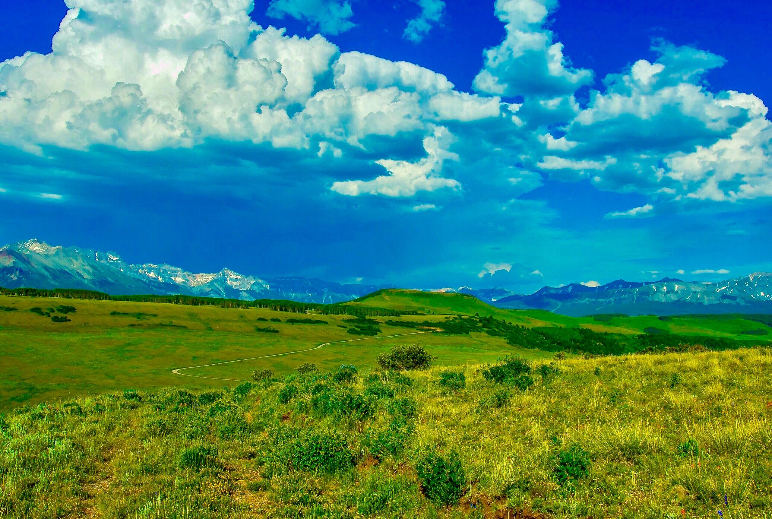 Open grassy land with rolling hills and a distant mountain range beneath dramatic clouds.