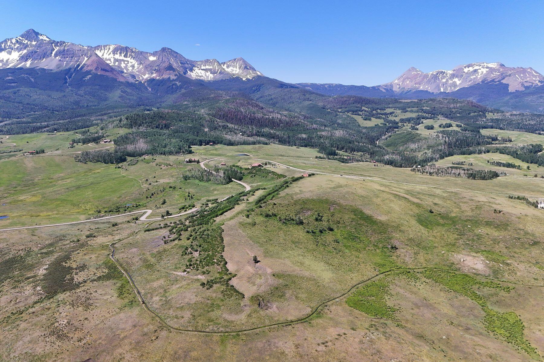 Aerial view of open land and winding roads beneath a broad range of snow-patched mountains.
