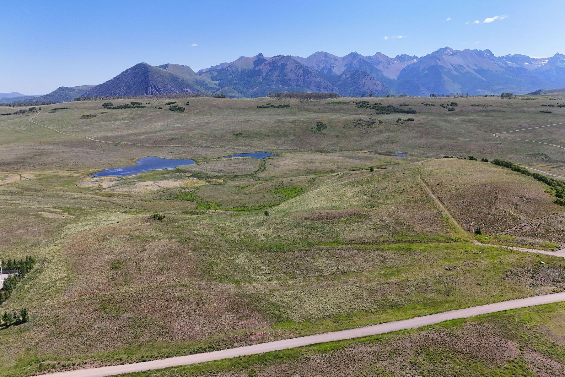 Aerial view of open land with a pond and mountain range beyond.