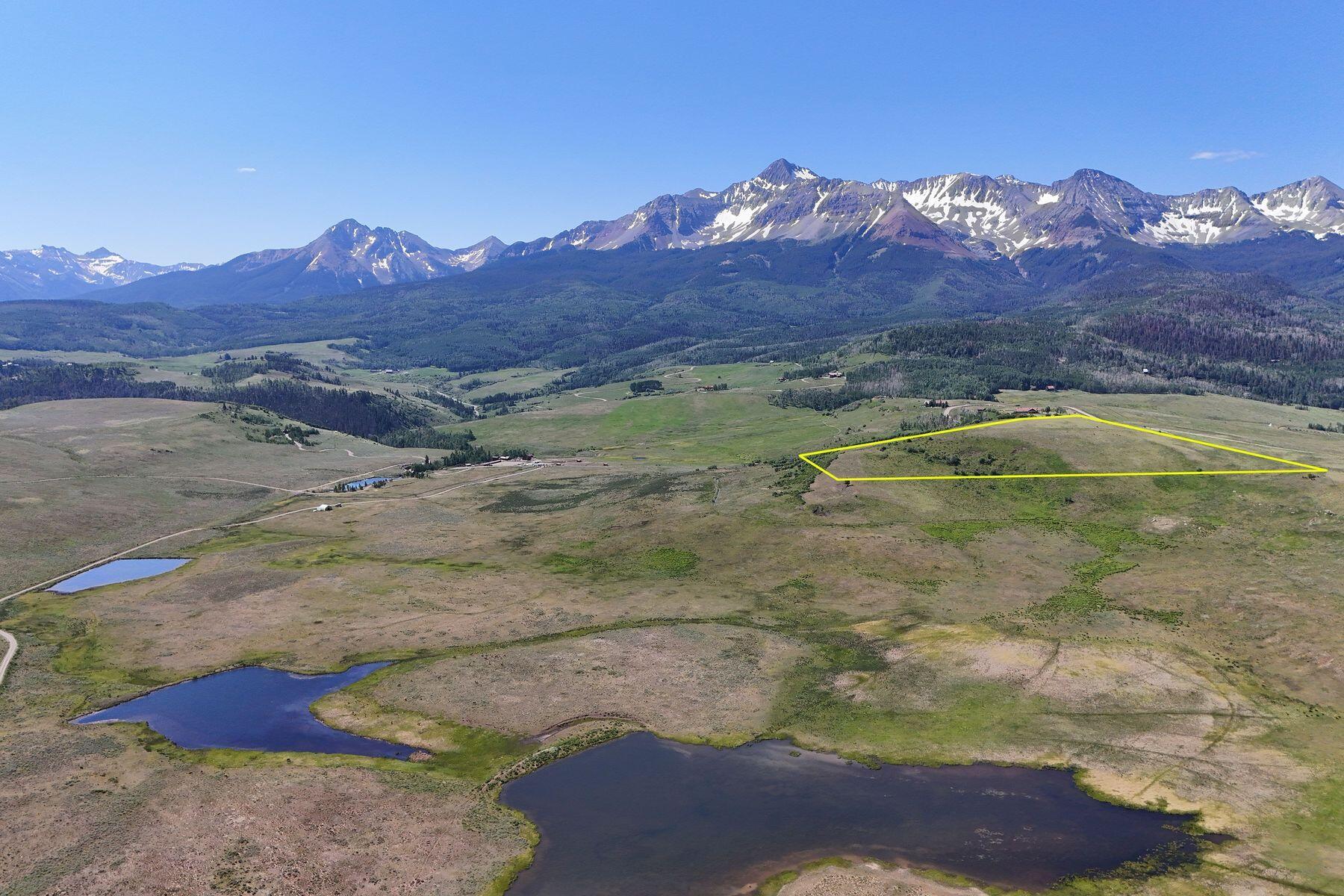 Aerial view of land outlined in yellow, with ponds and a snow-dusted mountain range in the distance.