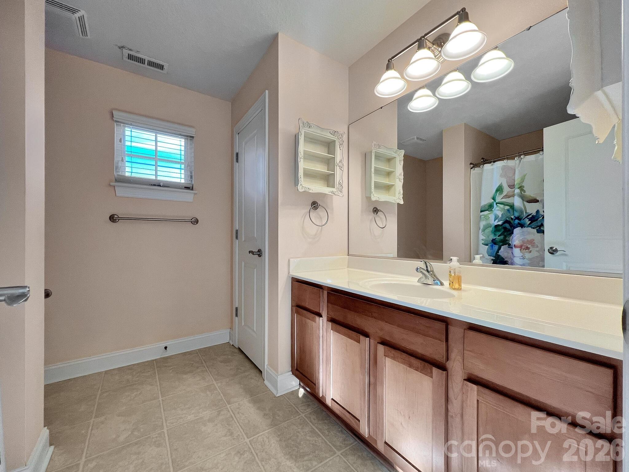 Bathroom with a long wood vanity, large mirror, tiled floor, and floral shower curtain.