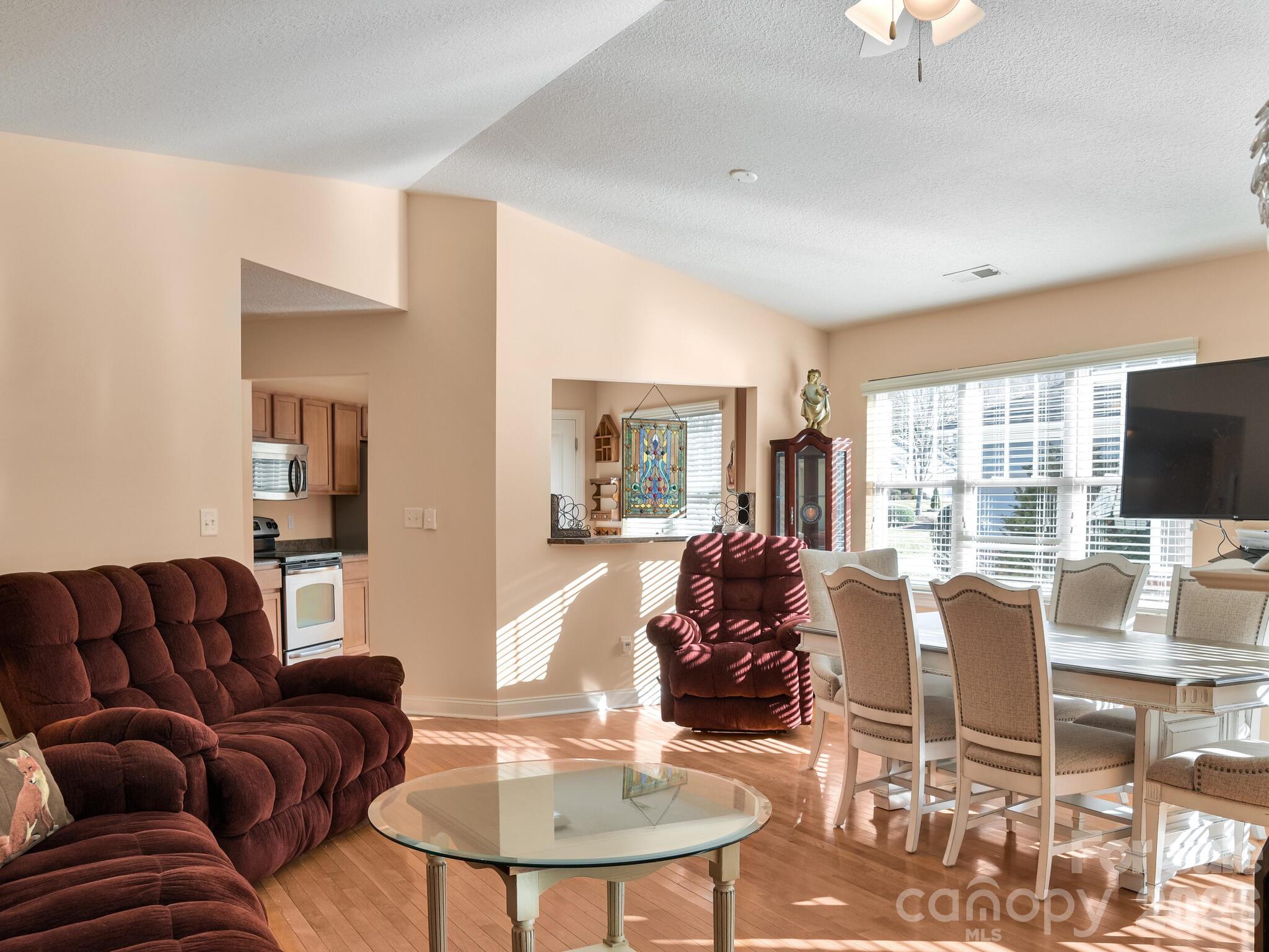 Open living and dining room with hardwood floors, burgundy seating, and large sunlit windows.