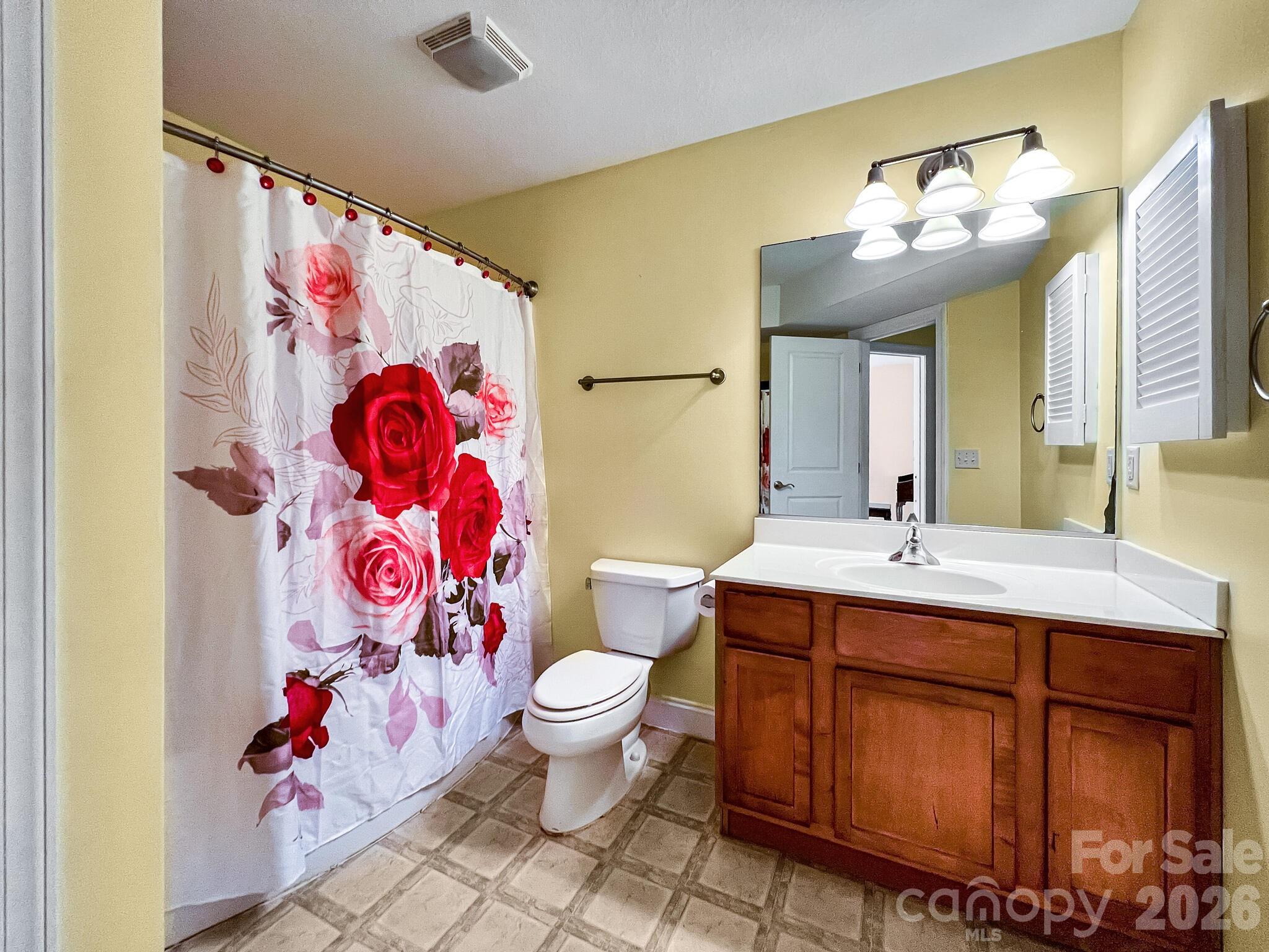 Bathroom with a rose-print shower curtain and a wood vanity with a wide mirror.