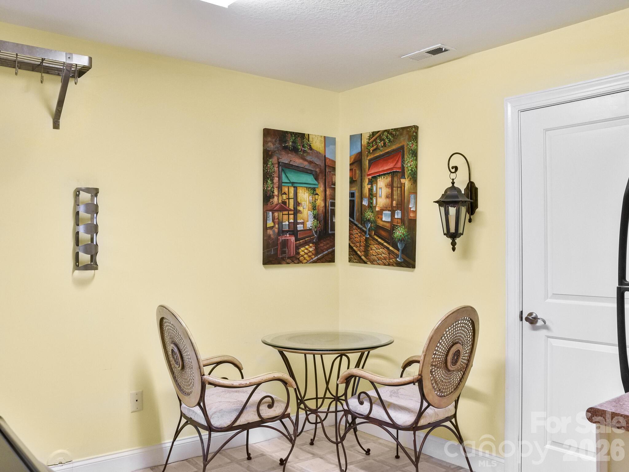 Dining nook with two ornate chairs, a round glass-top table, and colorful wall art.