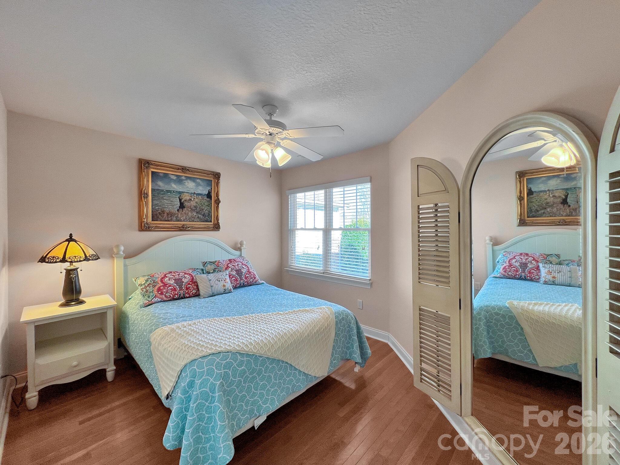 Furnished bedroom with a blue patterned bedspread, wood floors, and a full-length arched mirror.