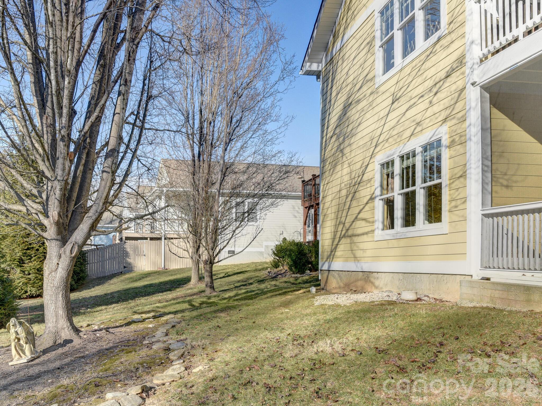 Yellow-sided home beside a sloping yard with leafless trees and a stone-edged path.