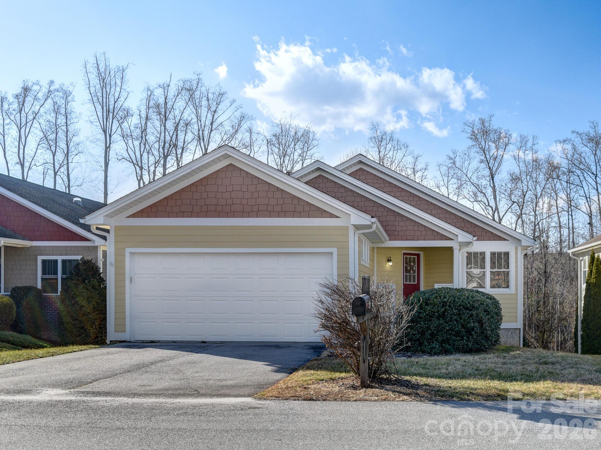 Front exterior of a single-story home with a double garage, red entry door, and leafless trees.