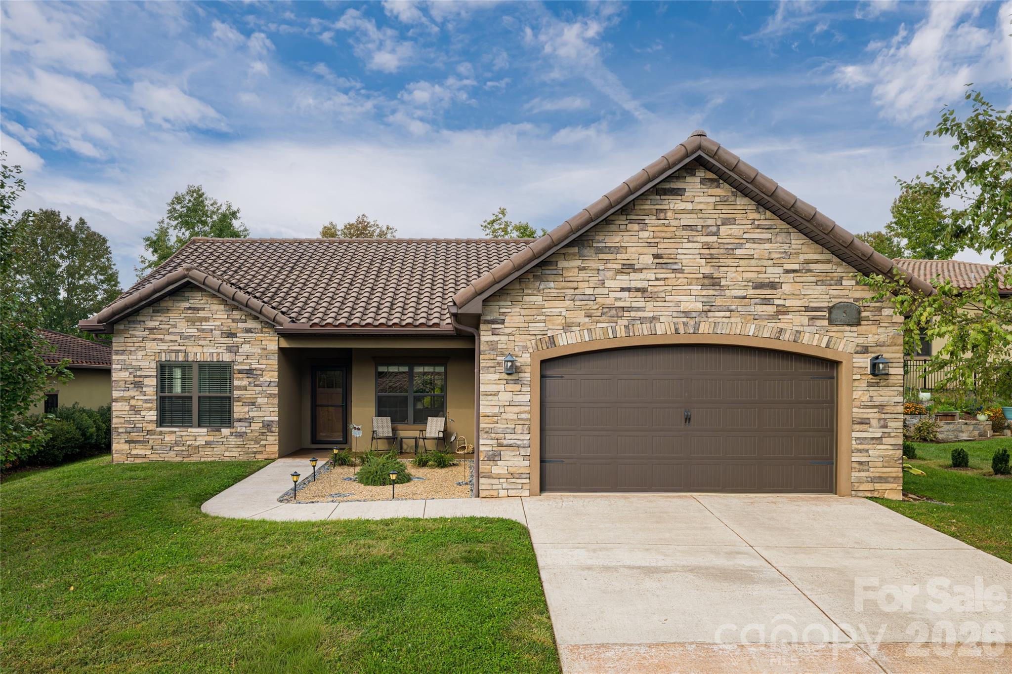 Stone-front single-story home with a covered entry, wide garage, and landscaped lawn.