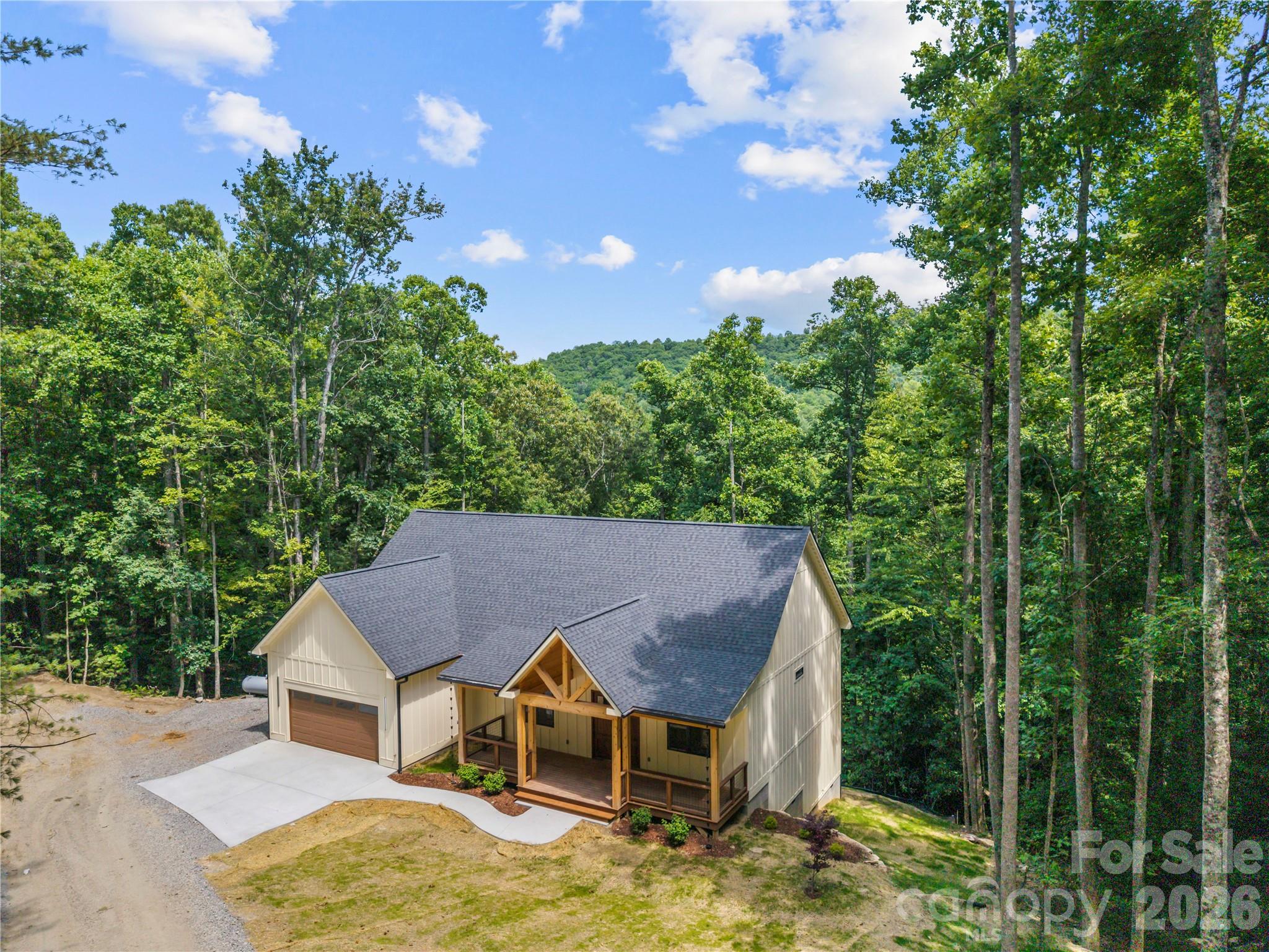House with a broad gray roof and timber porch, surrounded by dense woods.