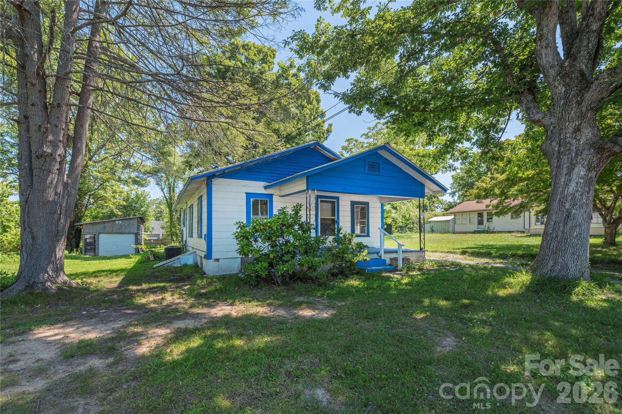 White house with bright blue trim and porch, framed by mature trees and a detached garage.