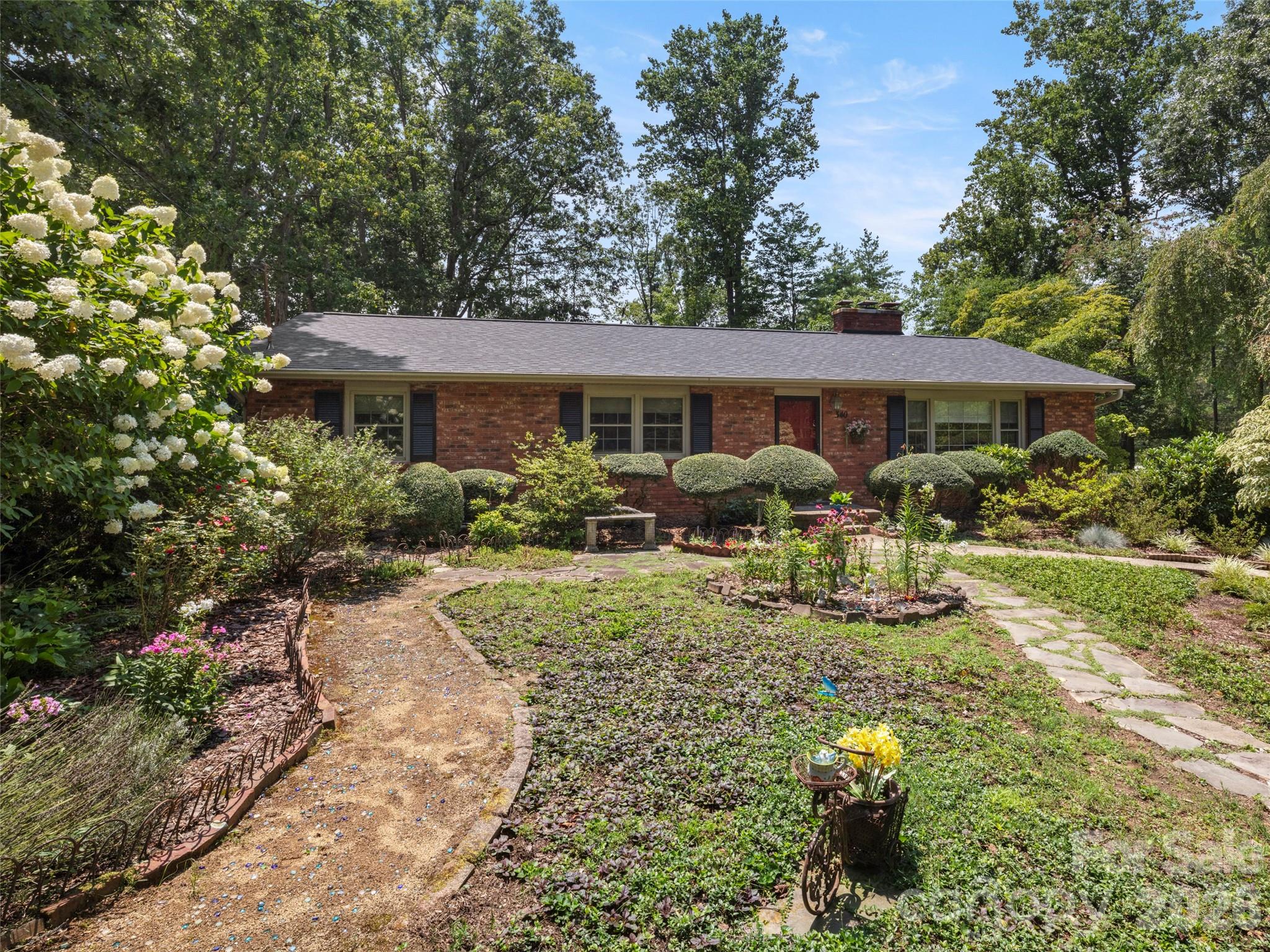 Single-story brick ranch house with a red door and a landscaped garden of flowering plants and shrubs.