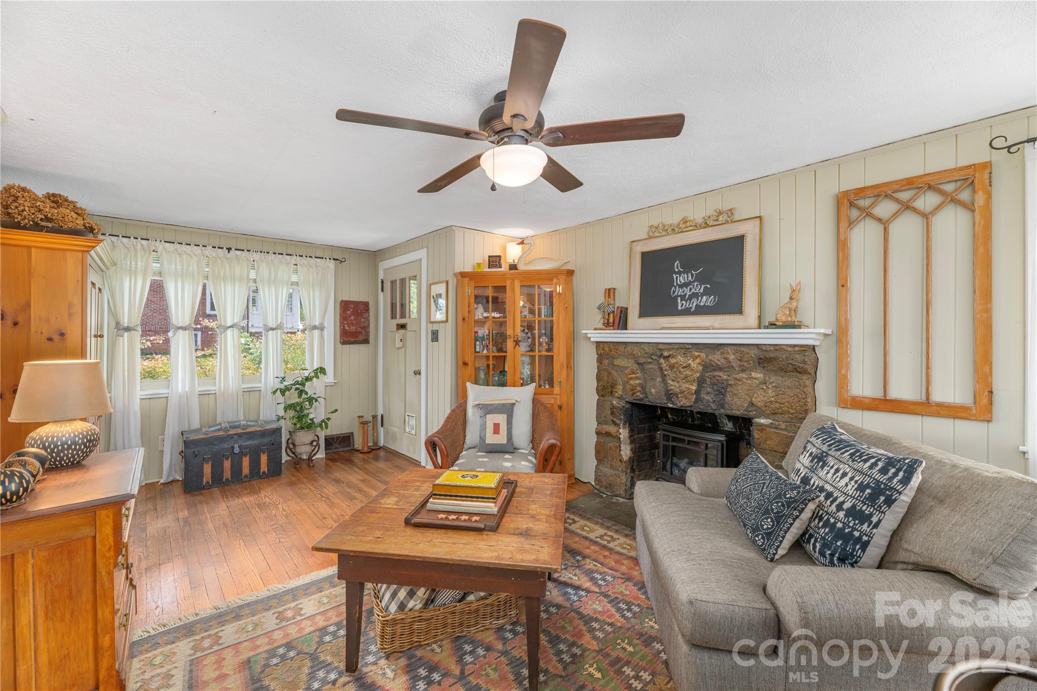 Living room with a stone fireplace, gray sectional, and wood floors.