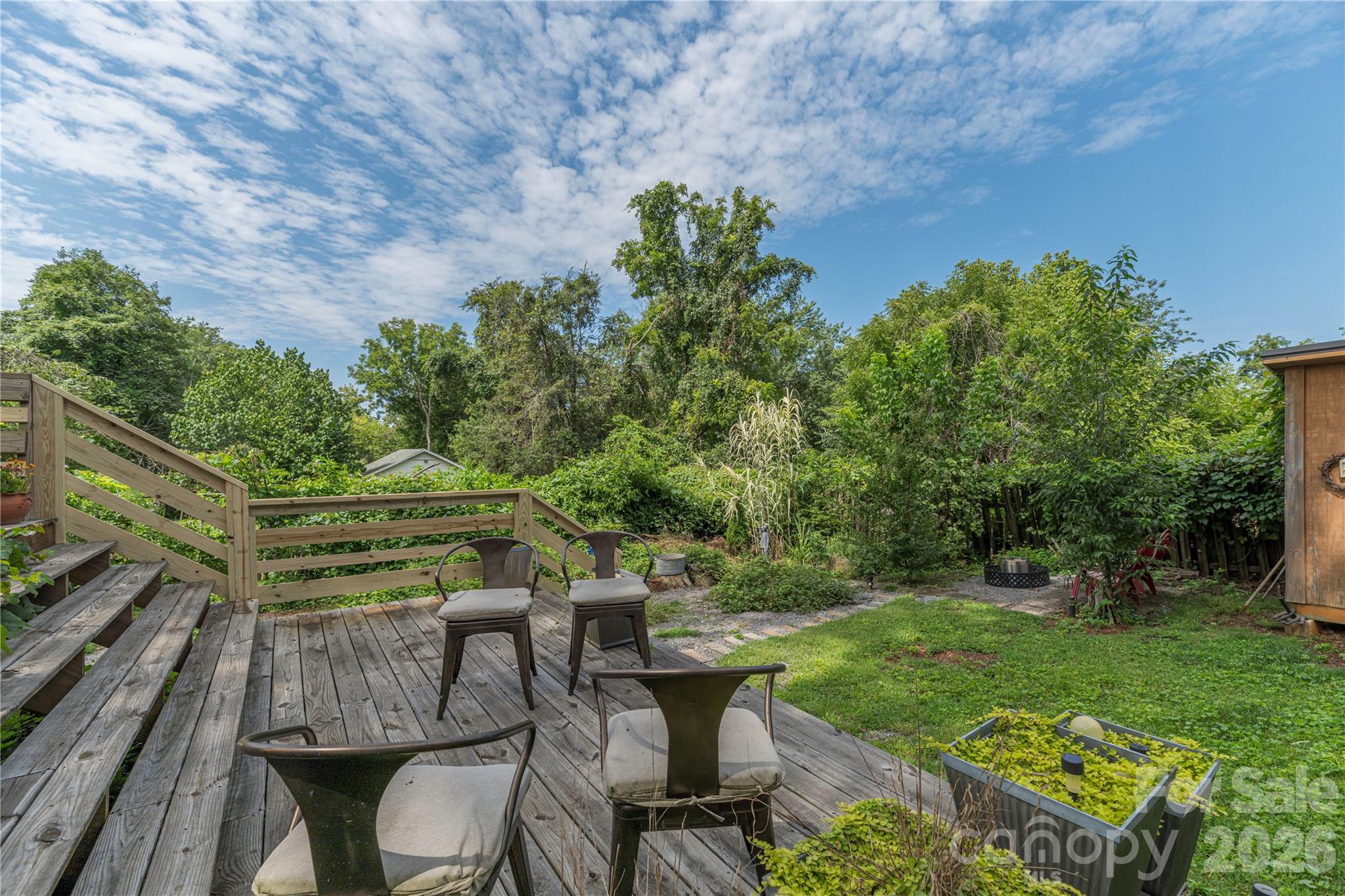 Wooden backyard deck with outdoor chairs overlooking a leafy garden and small lawn.
