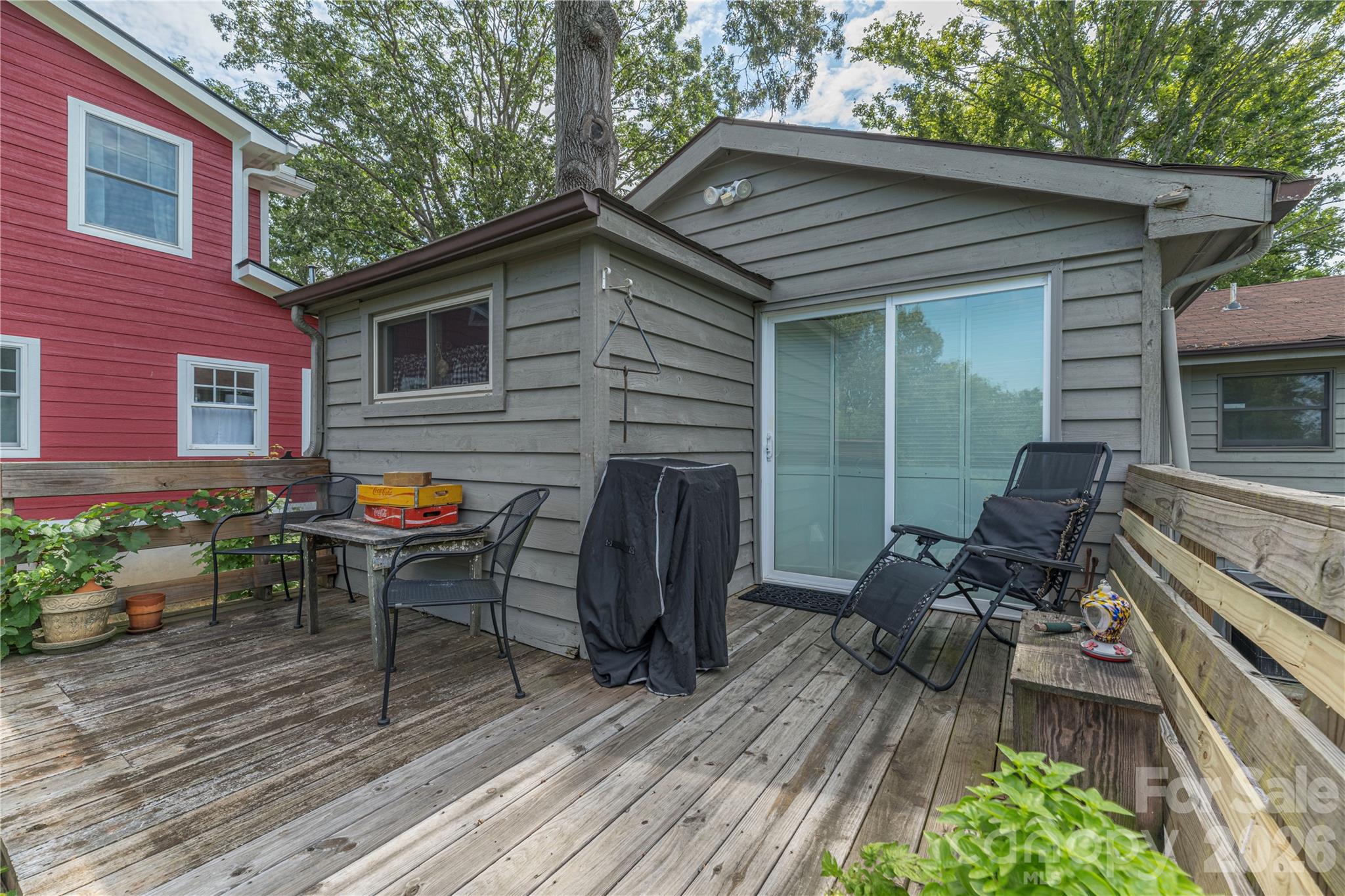 Wooden deck with lounge chairs, dining set, and covered grill beside gray-sided home.
