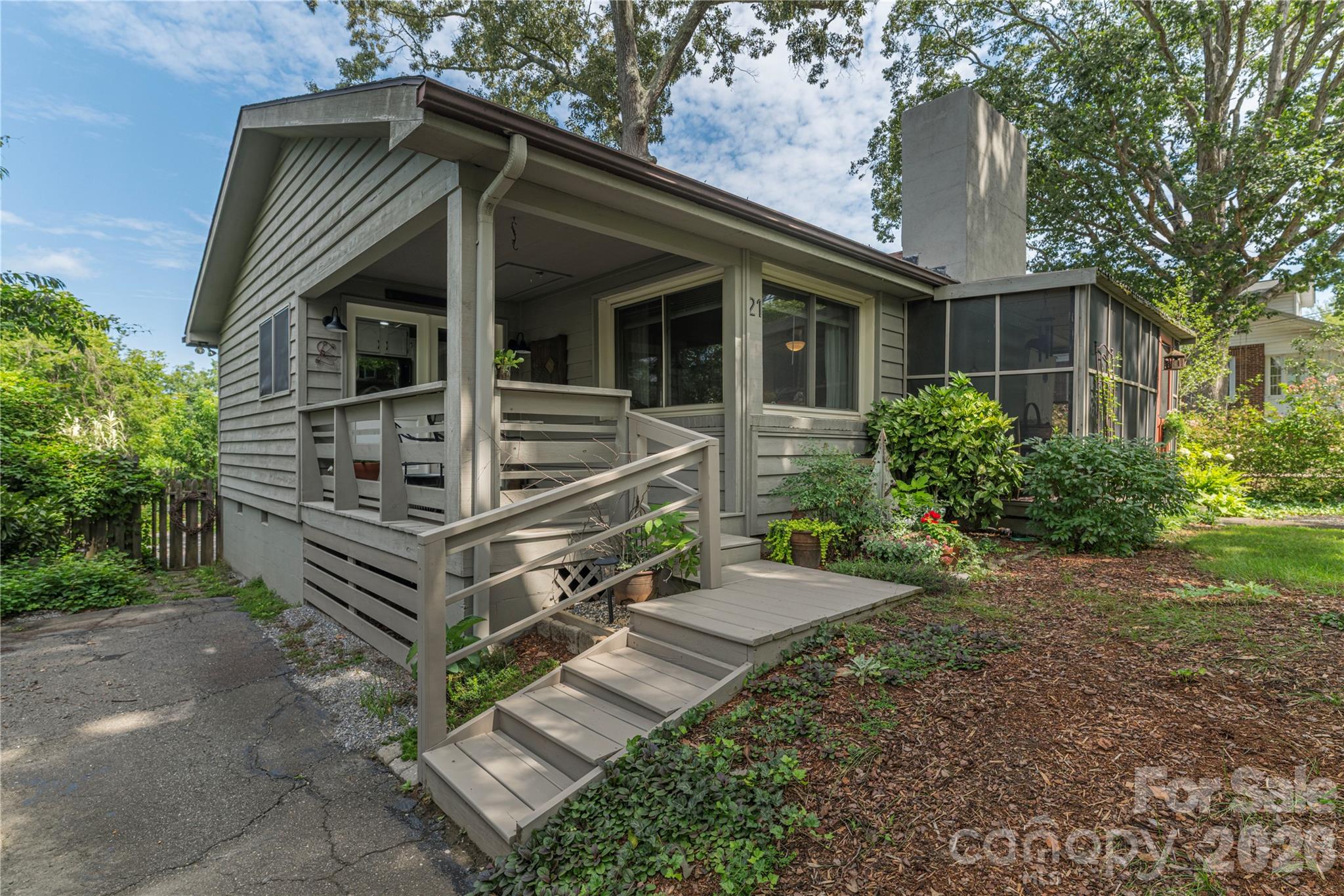 Gray-sided home with a covered porch, screened side porch, and wide steps through a landscaped yard.